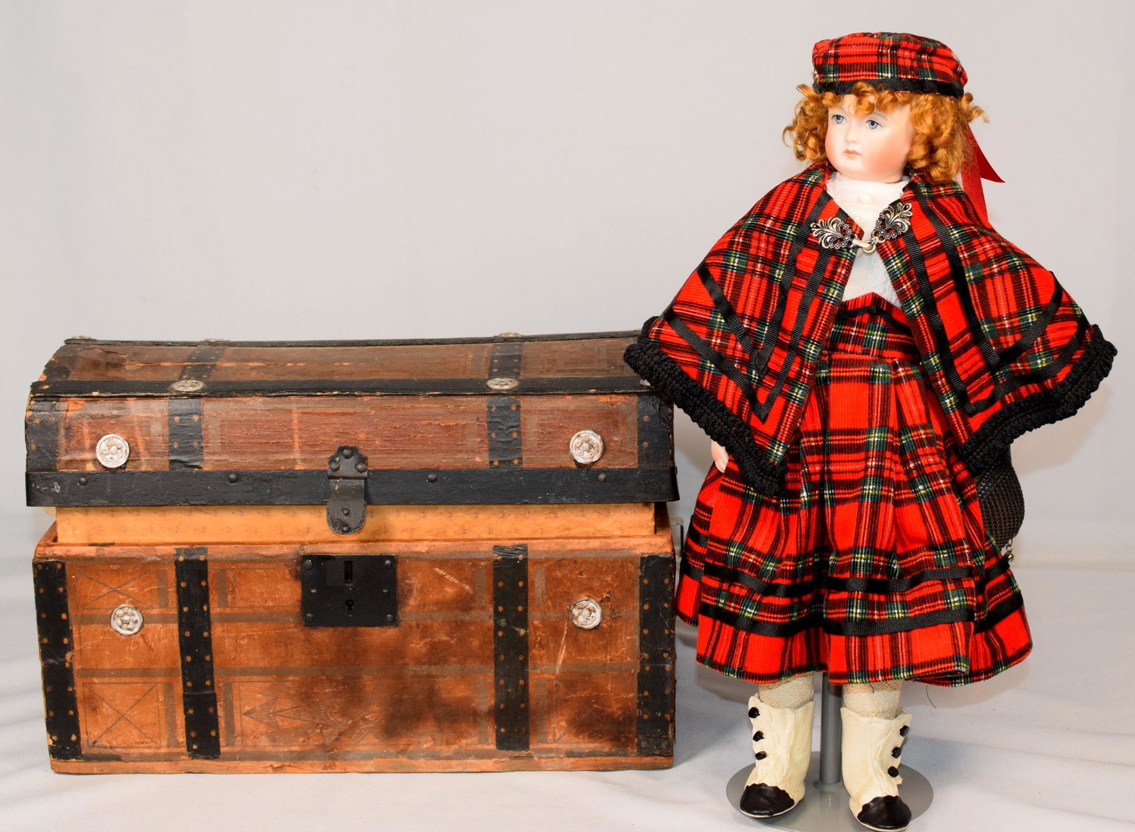 REPRODUCTION BISQUE HEAD DOLL AND ASSEMBLED TRUNK: 20th century reproduction bisque head doll with hand painted face ,blue eyes,blonde hair,bisque hands and cloth body. 16 inches tall on stand with red plaid dress and cape. Includes assembledtrunk wit