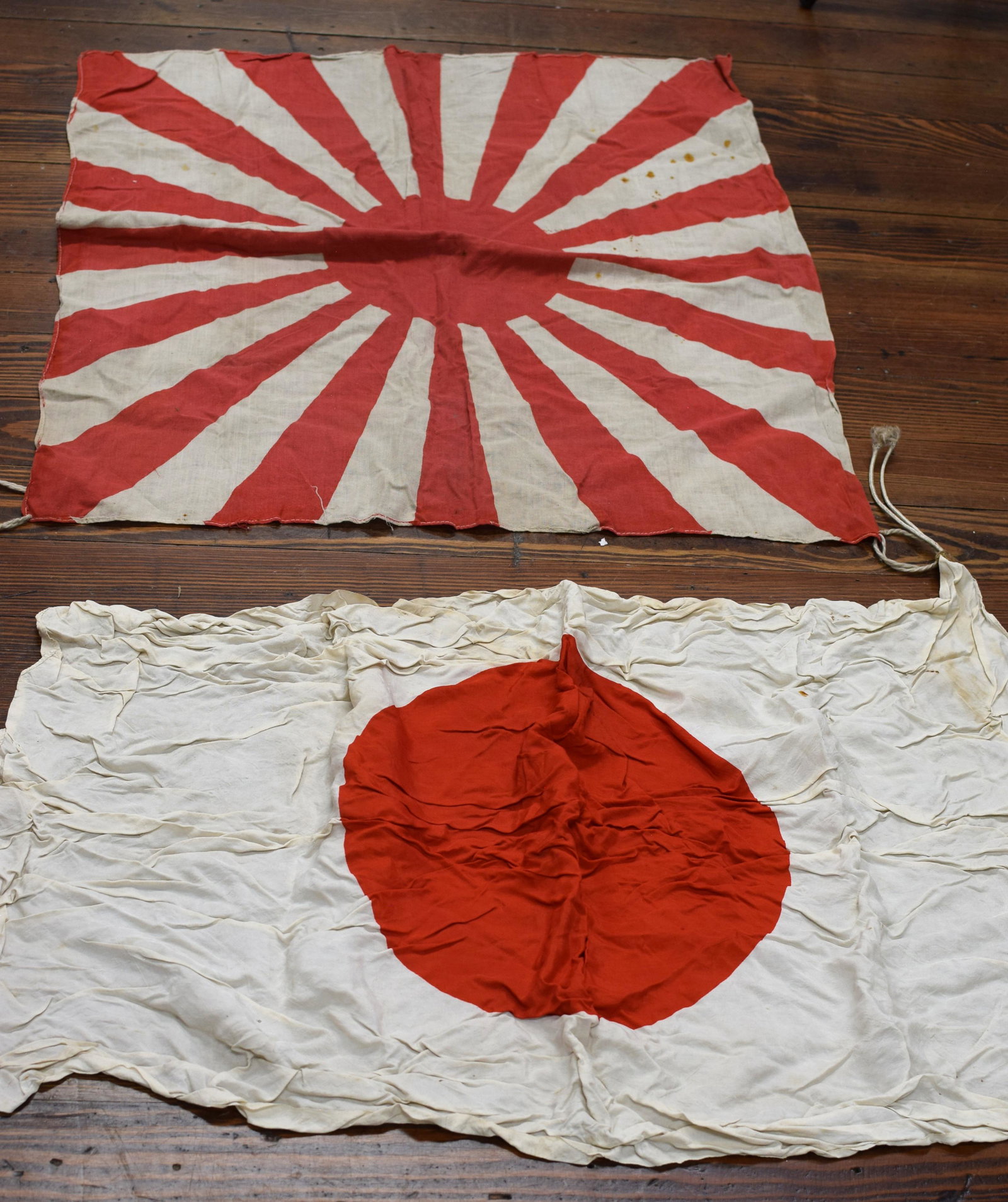 ON (2) JAPANESE WWII MILITARY FLAGS: Ca 1930-40's. 1) Japanese rising flag measuring 27 inches x 27 inches. Oiginal string holders. Some staining. Very small hole center. 2) Japanese meatball flag measuring 27 inches x 37 inches.Silk. Or