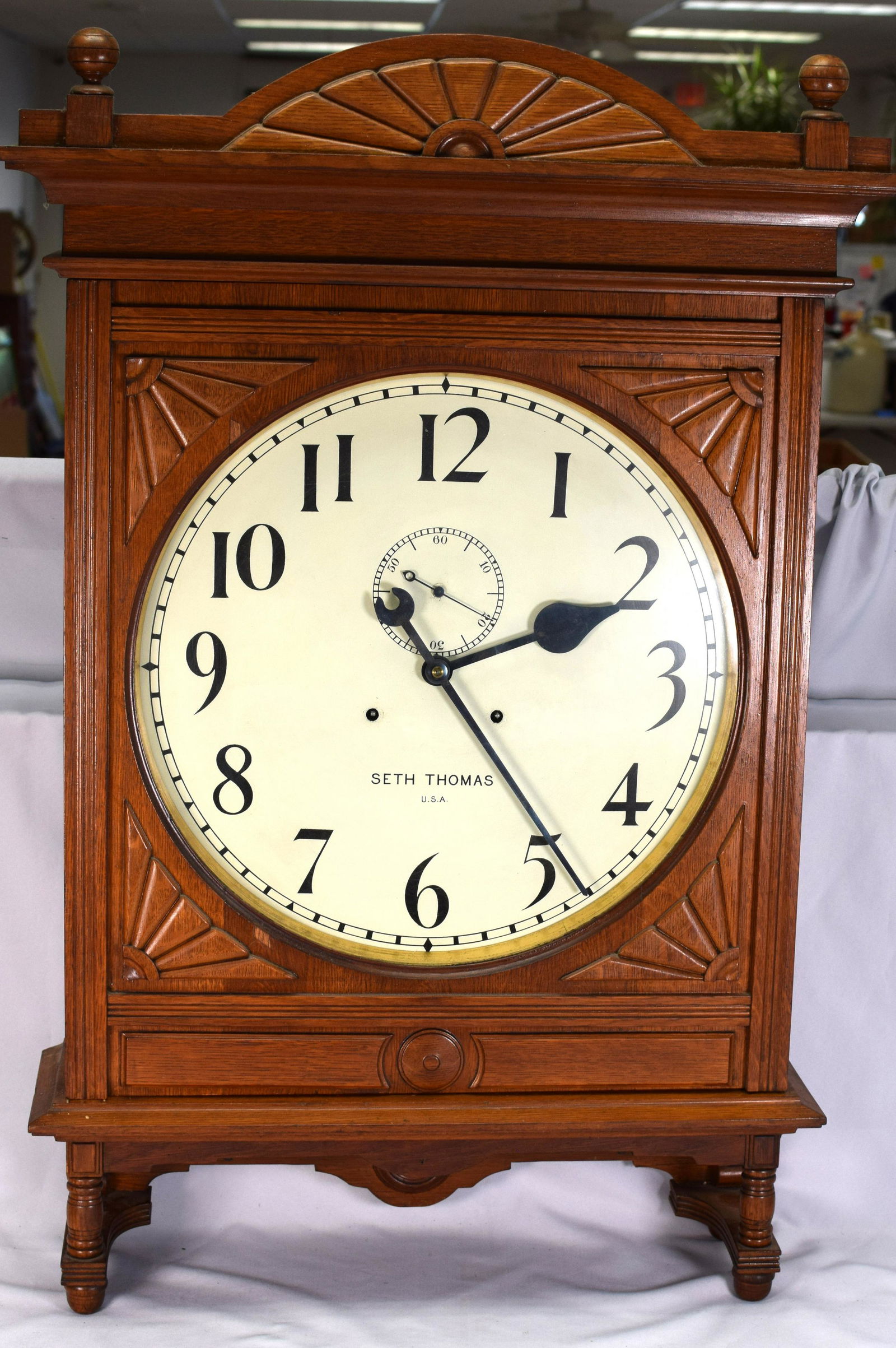 SETH THOMAS OAK OFFICE WALL CLOCK: Ca 1890/1910. Large Seth Thomas carved oak wall clock. Carved crest with ball finials. Carved foot/base with acorn finials. Carved fan decorated case. Measures overall 36 inches tall x 25 inches wide
