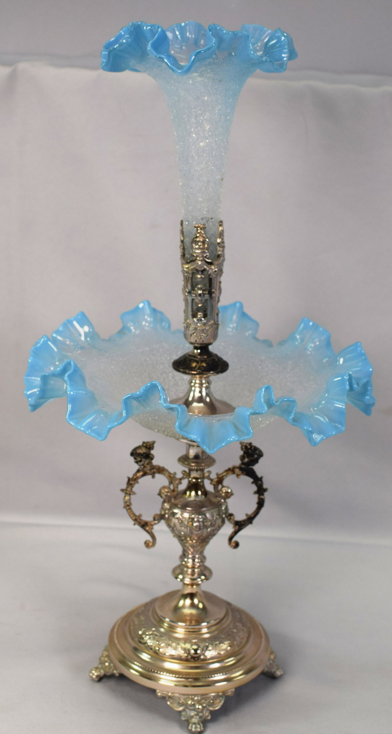 19TH SILVERPLATE SANDWICH CRACKLE GLASS EPERGNE: 19th Ornate footed and figural handle silverplate epergne. Sandwich glass. Ruffle edge blue opalescent glass center and center tulip vase. 19 inches tall x 9 1/2 inches diameter x 9 1/2inches. Good co