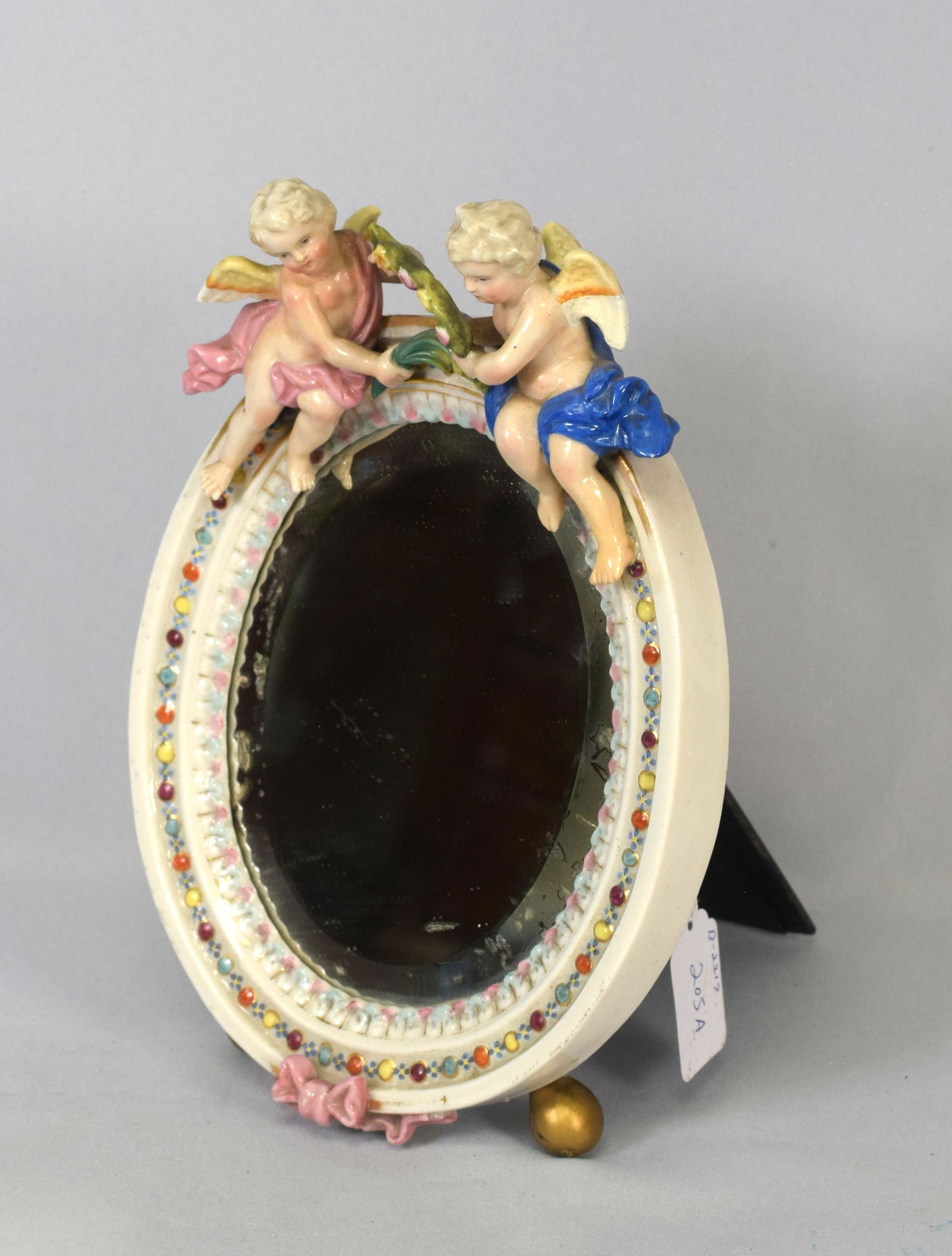 19TH MEISSEN DRESSING TABLE MIRROR: Meissen Dressing Table Mirror. Meissen cross-sword blue mark, oval mirror depicting a pair of putti holding garland. easel back stand. 9.5 inches in height. Shipping 3 pounds.
