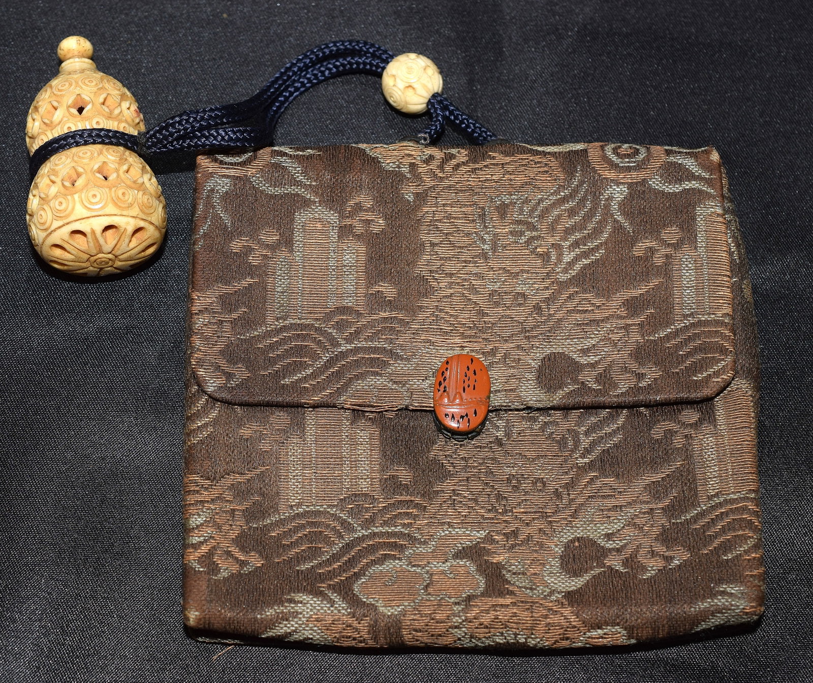 JAPANESE TOBACCO POUCH WITH CARVED OJIME: Japanese tobacco pouch,possibly silk with dragon design and enameled lady bug closure and a carved and pierced bone ojime in the shape of or snuff bottle. Good condition, some minor wear on fabric. Po
