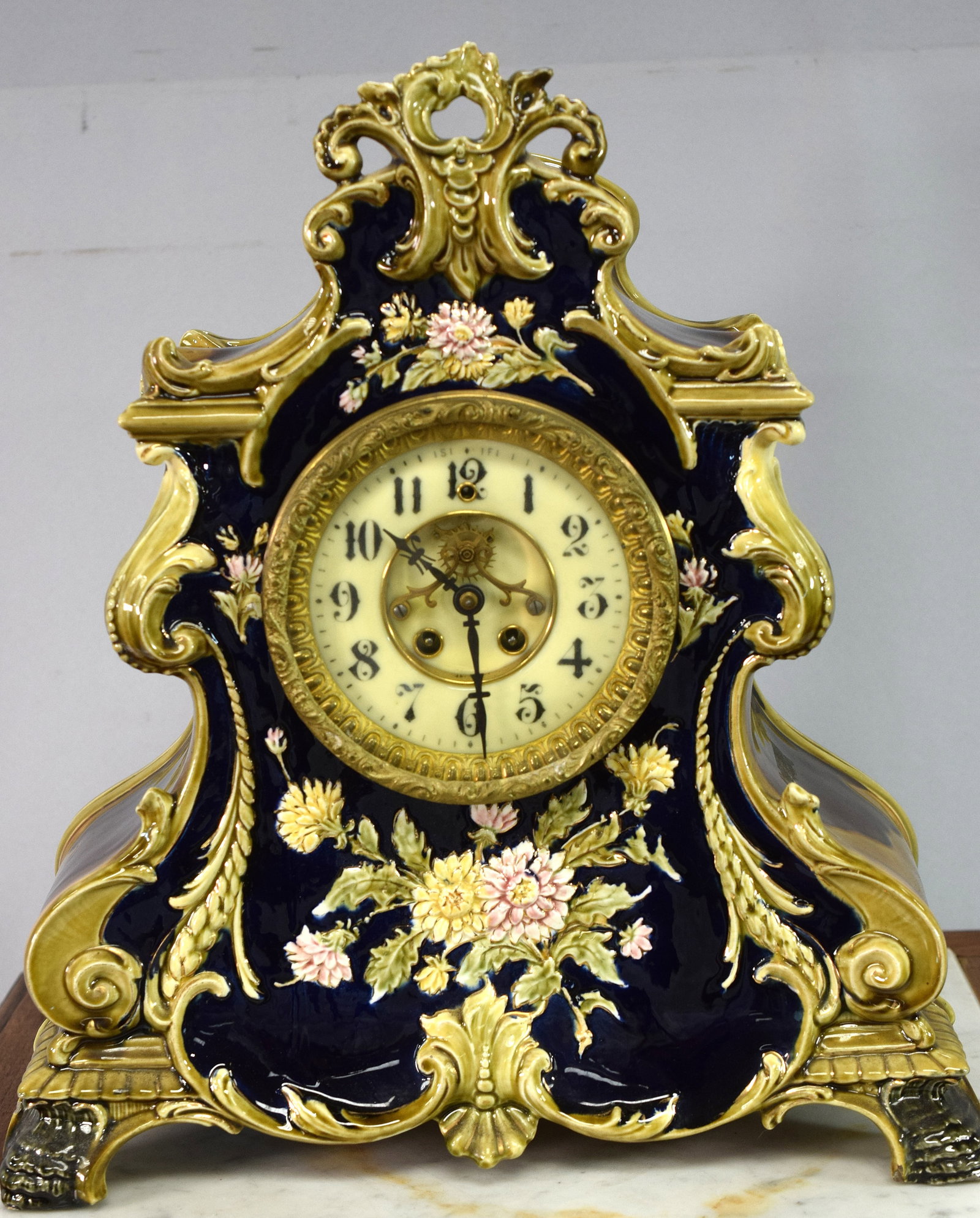 LARGE ORNATE GILBERT MAJOLICA MANTLE CLOCK: Wm. Gilbert Co. Fancy Majolica porcelain Mantle clock. Open escapement porcelain face. Deep gloss navy blue front. Serpentine sides, crest top in moulton glaze in browns and golds. Molded floraldecora