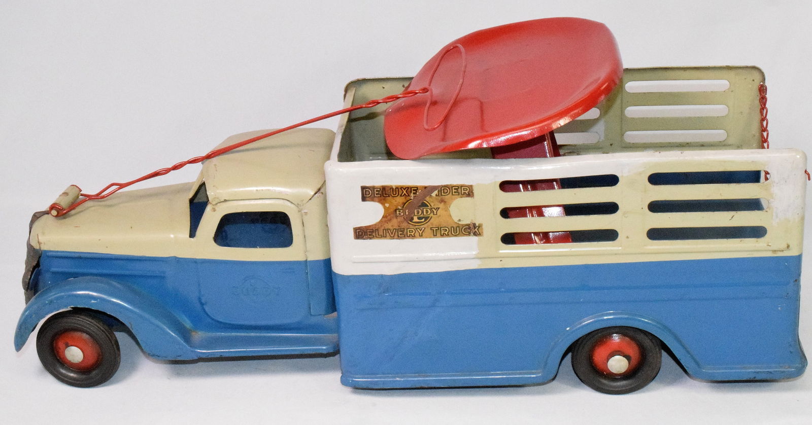 BUDDY L DELUX RIDER DELIVERY TRUCK: Buddy L Delux Rider delivery truck in pressed steel with removable red riding seat seat, rubber wheels and red pull handle, original label on side and insignia on door. Good condition, some wearand re