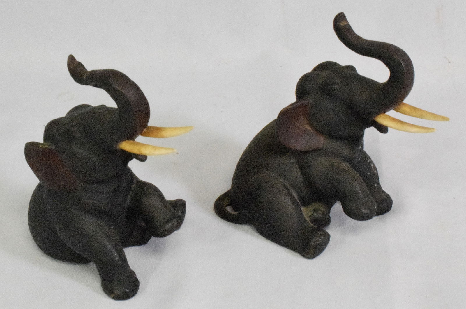 JAPANESE SIGNED BRONZE SEATED ELEPHANTS: Ca 19th/20th century. Meiji period. Either figures or bookends. Bone tusks. Cold painted ears and mouth. Seated pose with trunk raised. Original dark patina. One has the Japanese or Chinesescript mark