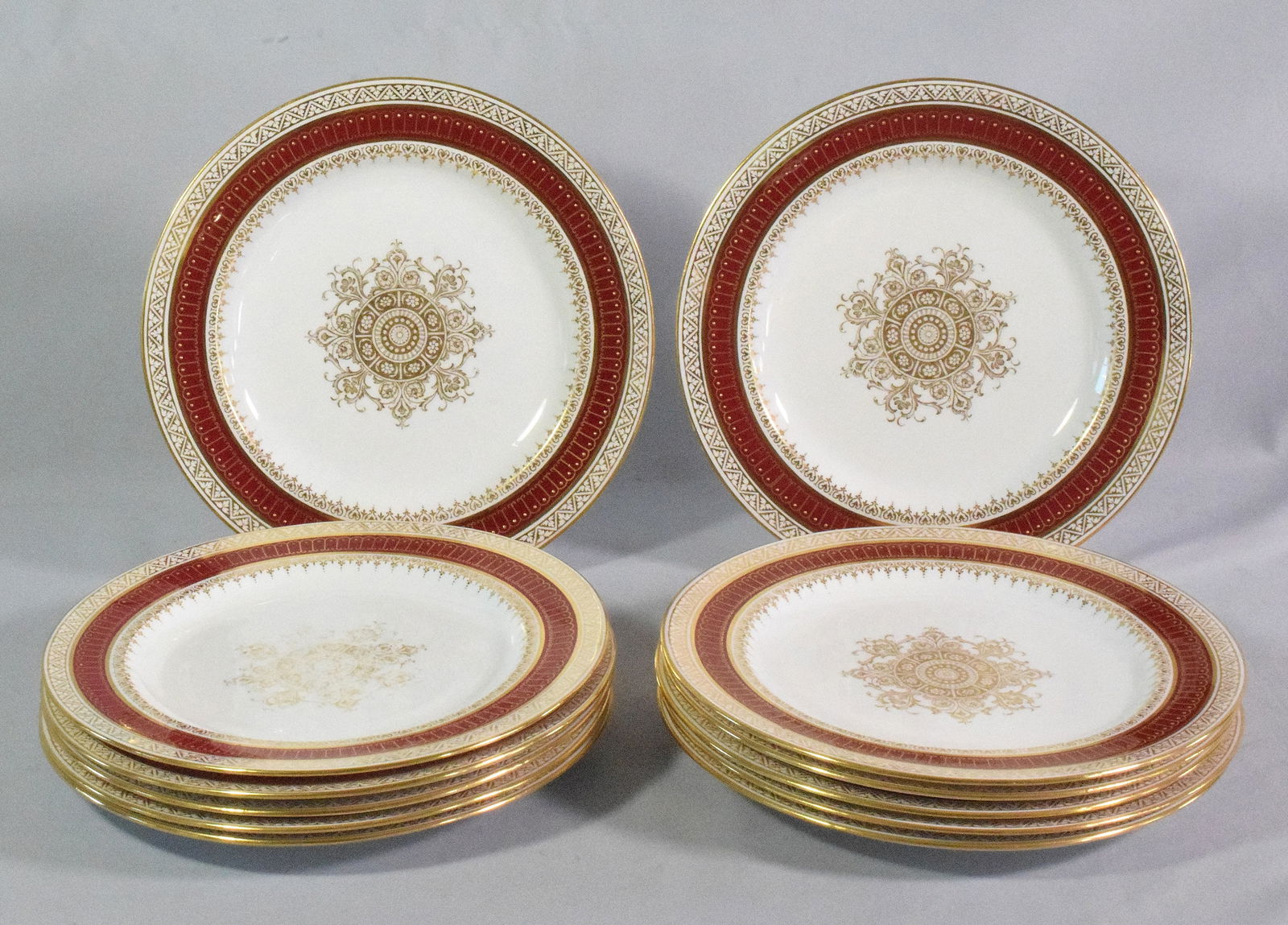 12 PIECE WEDGWOOD PORCELAIN DINNER PLATES: Cream or off white ground with gold and burgundy rim with gold decoration in center of plates. ( Two plates show wear in center of plates)10 plates showing light use and in good condition. 10inches pl