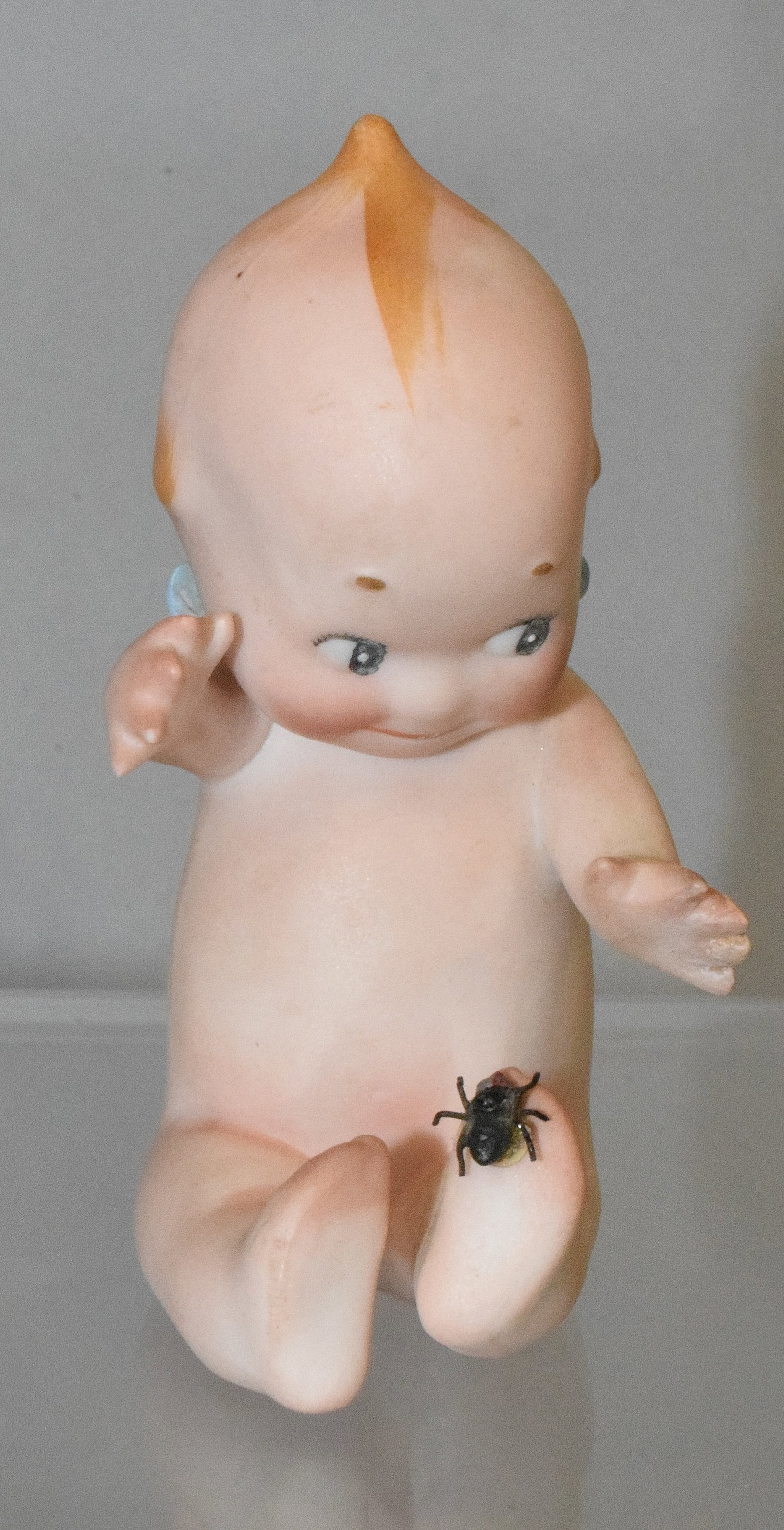 KEWPIE WITH SPIDER: all-bisque with classic Kewpie features and blue wings. 3? Kewpie with turned up right foot with black spider on bottom of foot; C in circle mark on bottom. Good condition.