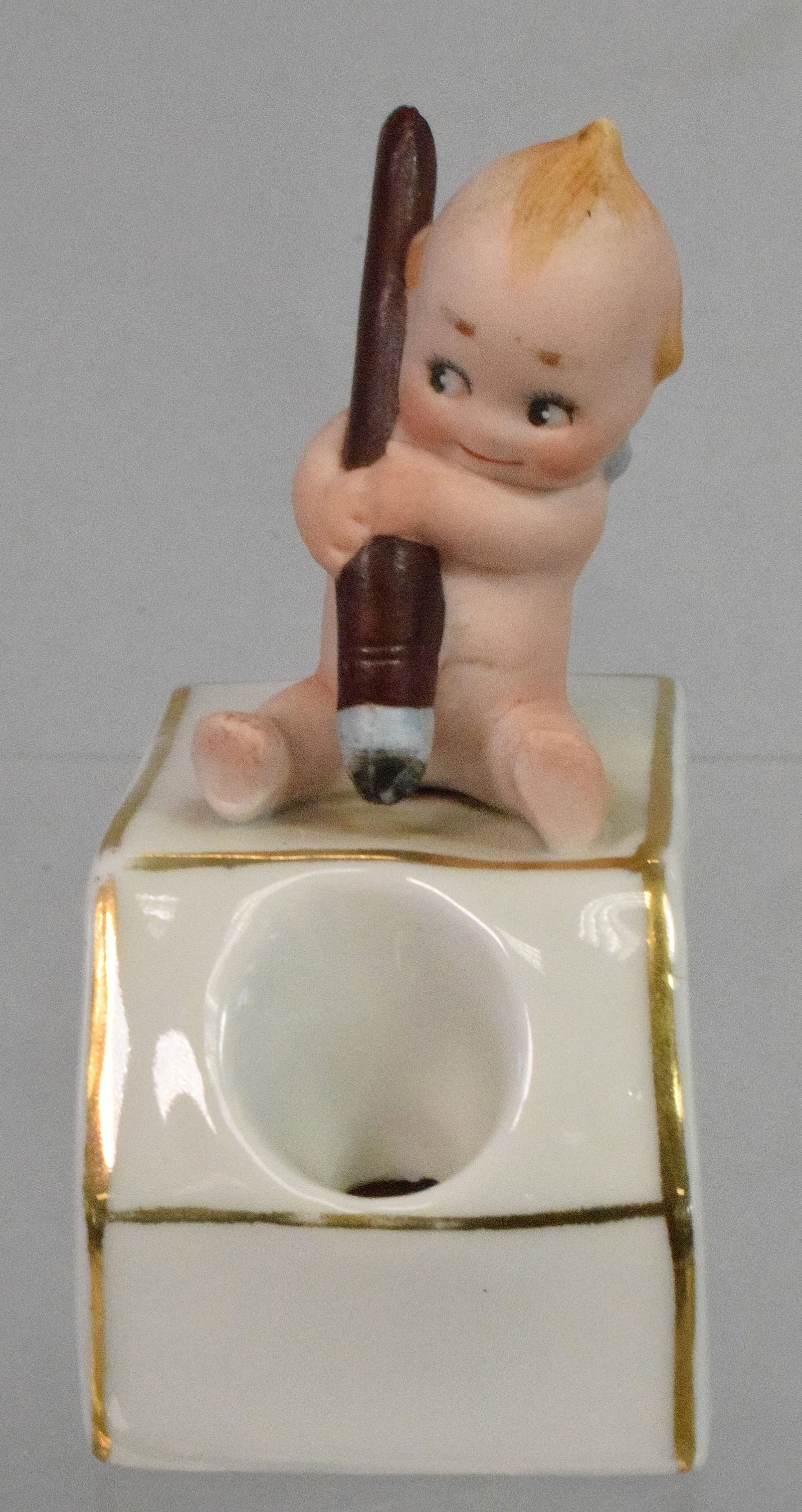 BISQUE KEWPIE WITH PEN ON INK WELL.: Figure all bisque on top of porcelain inkwell. 3 1/4 tall Good condition.