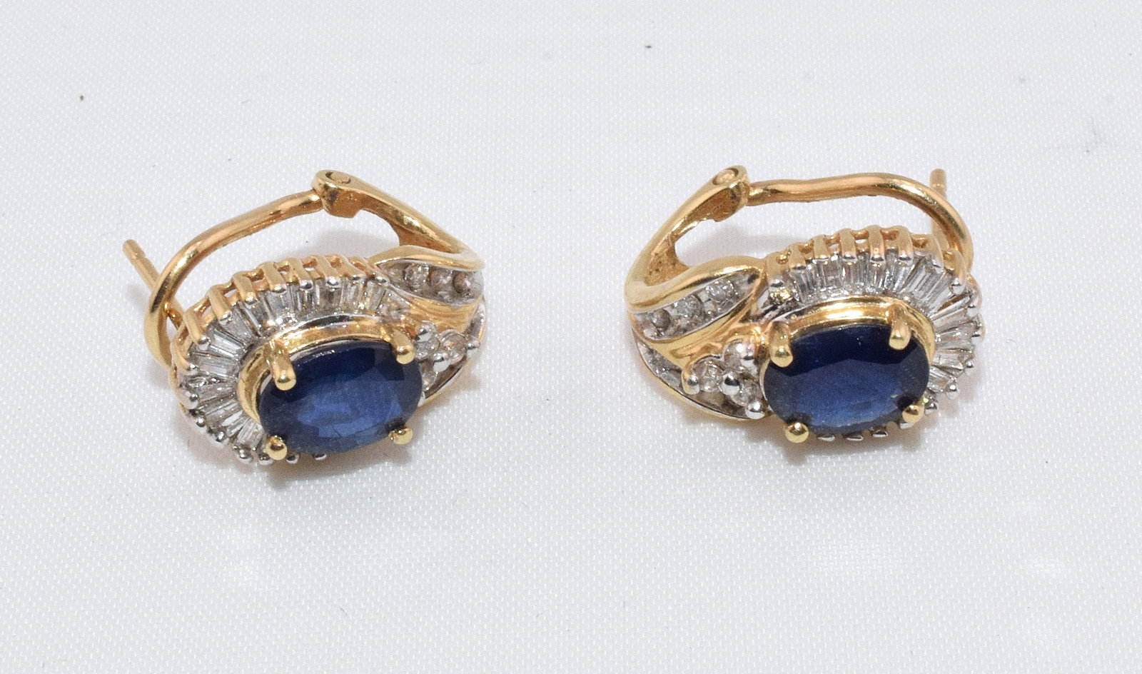 14K DIAMOND AND SAPPHIRE EARRINGS: Pair of 14k yellow gold earrings with an oval cut sapphire center stone (not sure if natural or synthetic) approx. 3/4 ct. surrounded by 18 baguette cut white diamonds, approx.1/32 ct. , and accented 