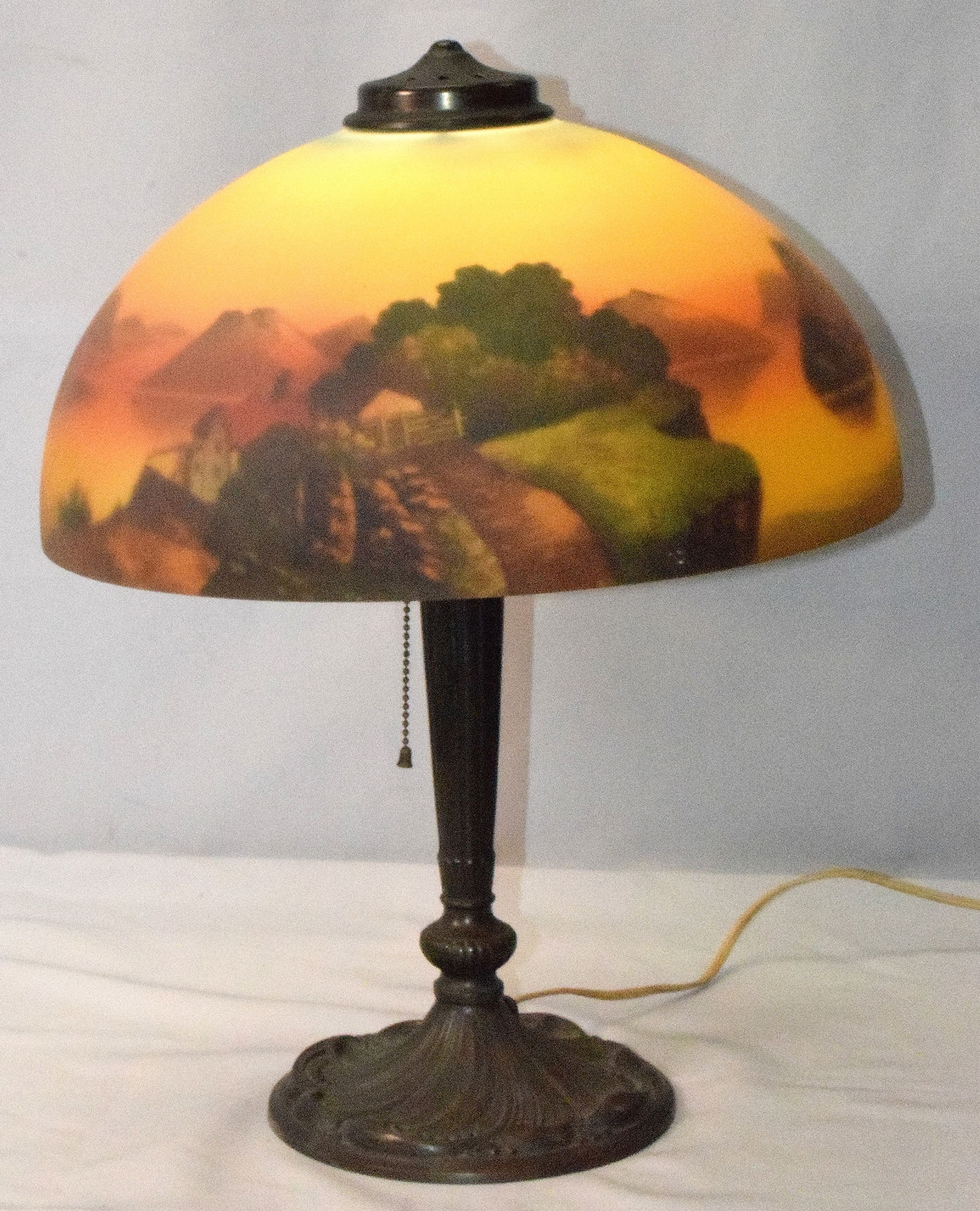 SIGNED PITTSBURGH REVERSE SUNSET PAINTED LAMP: Antique Pittsburgh Lamp Co. Signed reverse painted lamp. Shade signed on top rim. Based signed PLB & G Co. #2047. Detailed sunset mountain lake scene with house and fence. Base 7 1/2 inches diameter w