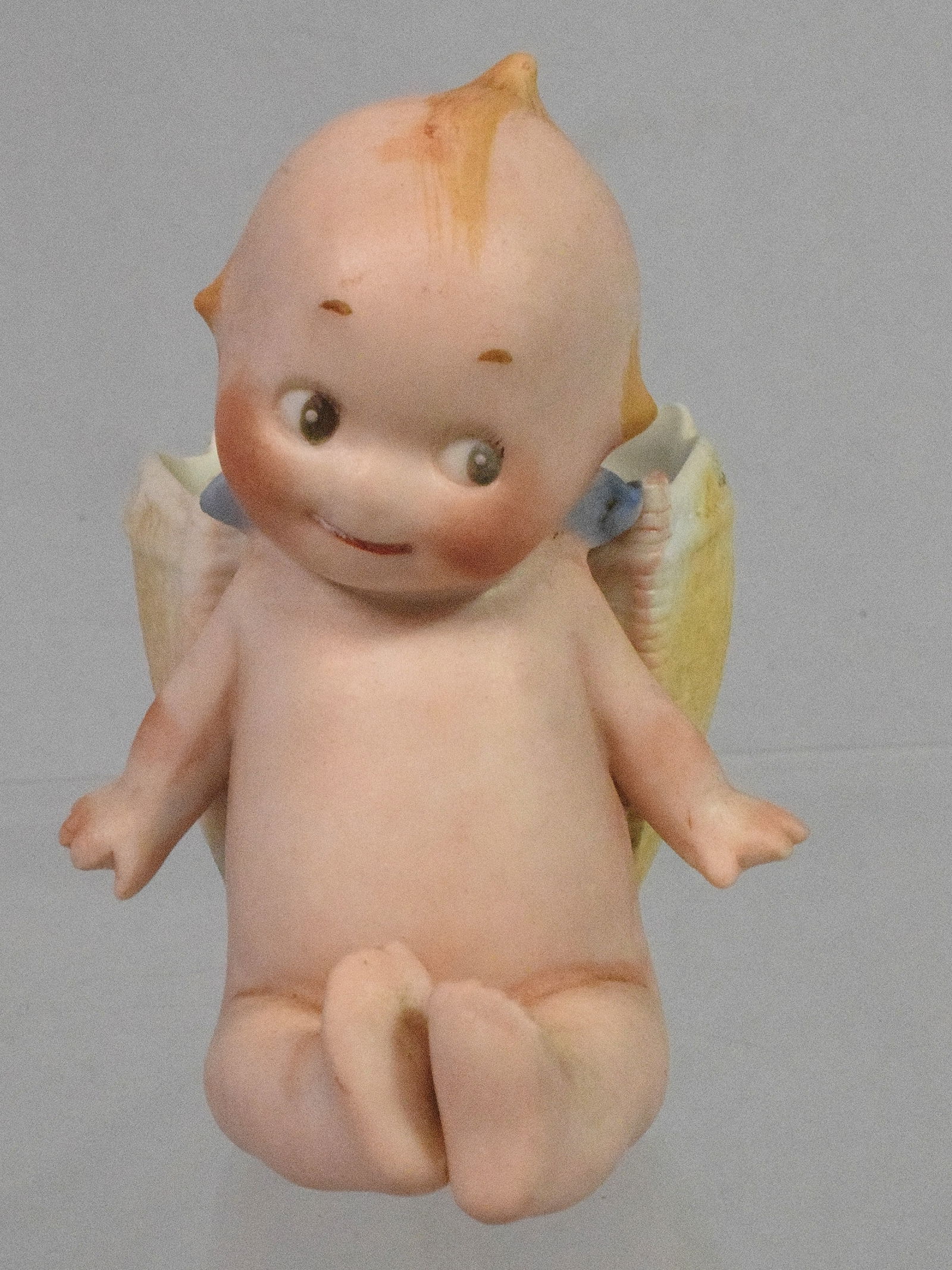 SEATED KEWPIE LEANING AGAINST A WOVEN BASKET. 3 ?: All bisque. Good condition.