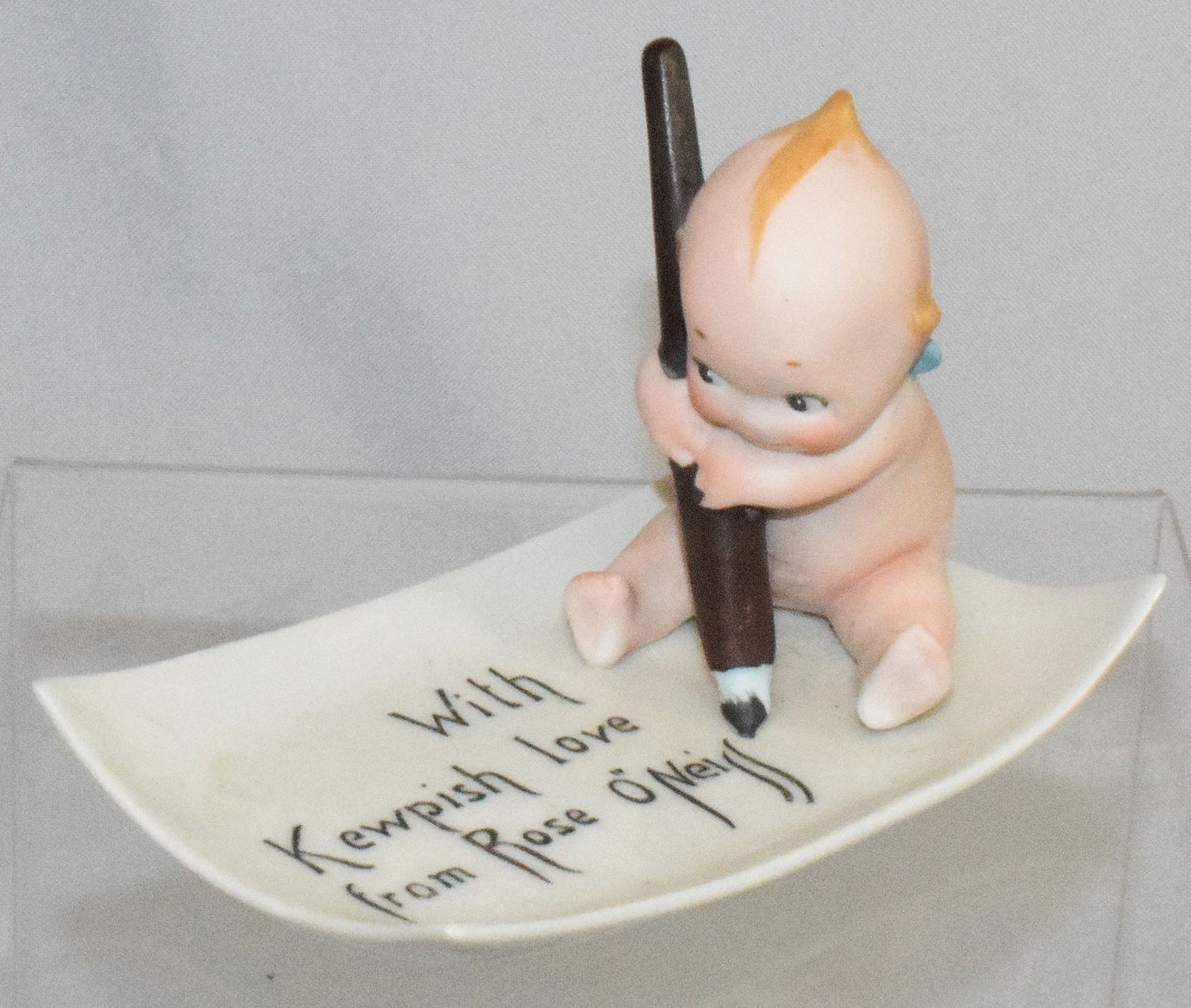 GERMAN BISQUE KEWPIE PEN AND TRAY WITH KEWPISH: Rose O'Neill Bisque Kewpie with pen on a porcelain 3" x 5" postcard reading "With Kewpish Love from Rose O'Neill". No stamp on it. Base with black stamp ? Good condition.