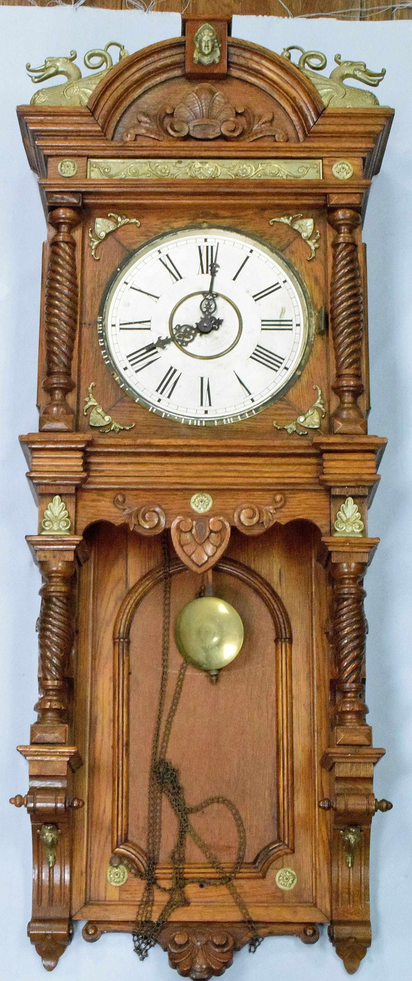 OAK WATERBURY AUGUSTA WALL CLOCK: A late antique 19th century Waterbury "Augusta" model carved oak wall clock. 8-day weight driven time and strike movement with silvered metal dial and Roman numerals. Fancy Oak case with brassornament