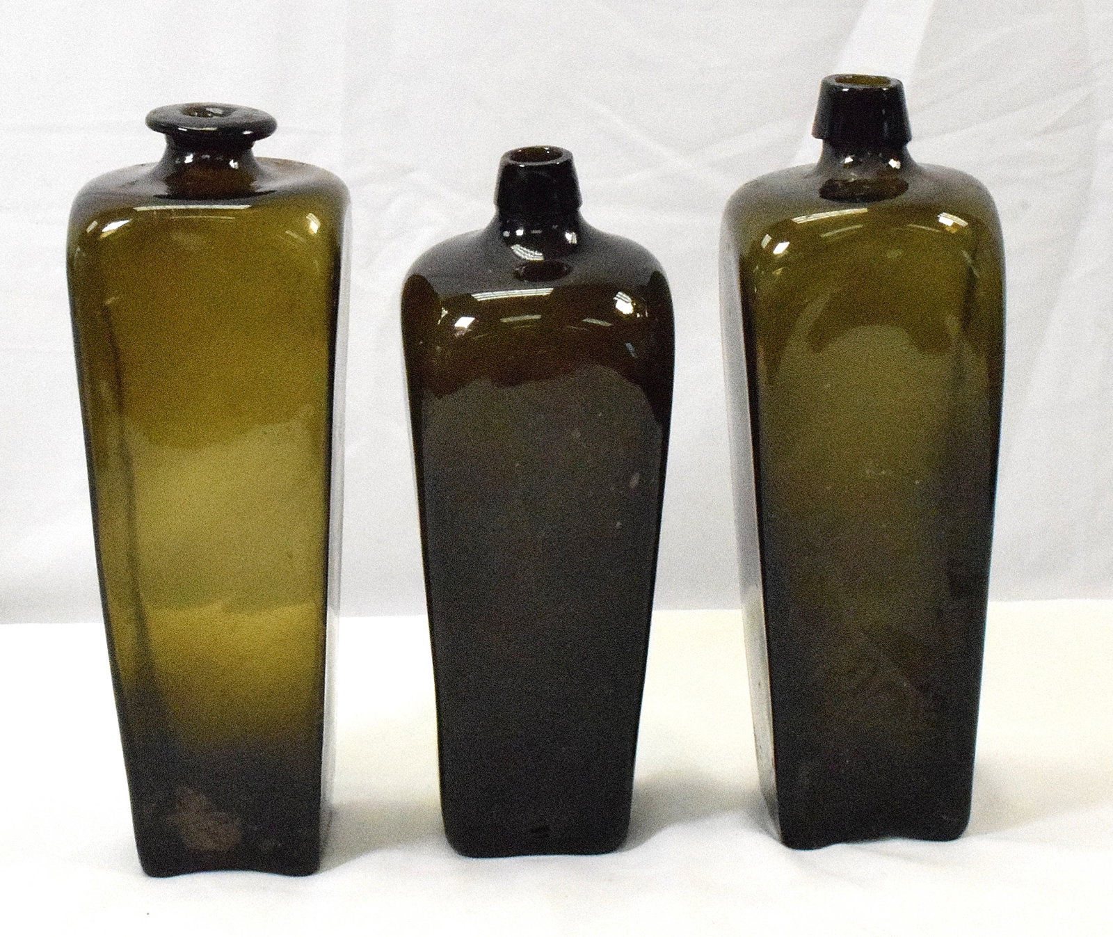 SET OF 3 GIN BOTTLES: Three olive glass gin bottles, dutch. One bottle is cracked on the lower side. Overall good condition. L: 11in, W: 4in, H: 11in, Weight: 5 lbs.