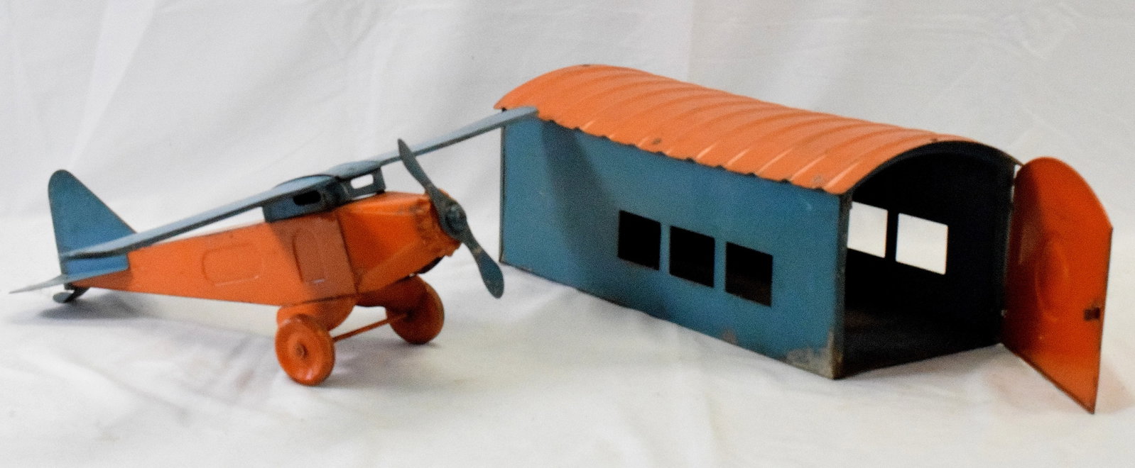1920'S GIRAD MATCHING HANGAR AND AIRPLANE: 1920's original pressed steel toy airplane with its matching hangar. Airplane has folding wings. Original painted colors or orange and turquoise. Overall good condition with normal play wear,scuffs, e