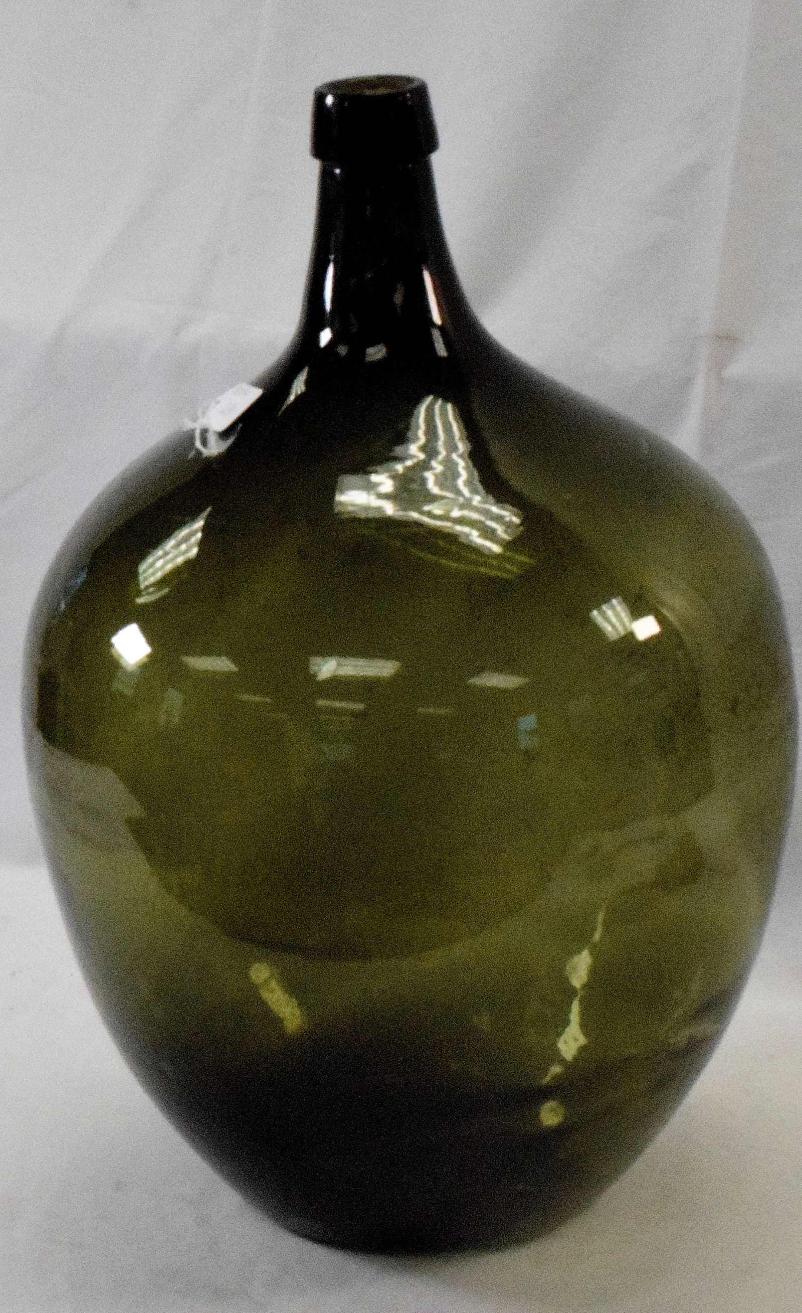 18TH/19TH DEMIJOHN GLASS BOTTLE: Early bottle shaped Demijohn bottle. Free blown glass, 21 1/2" Ht., approx. 14" W. Deep olive color. Demijohn bottles used for fermenting and transporting liquids like wine, beer, or oliveoil, they ar