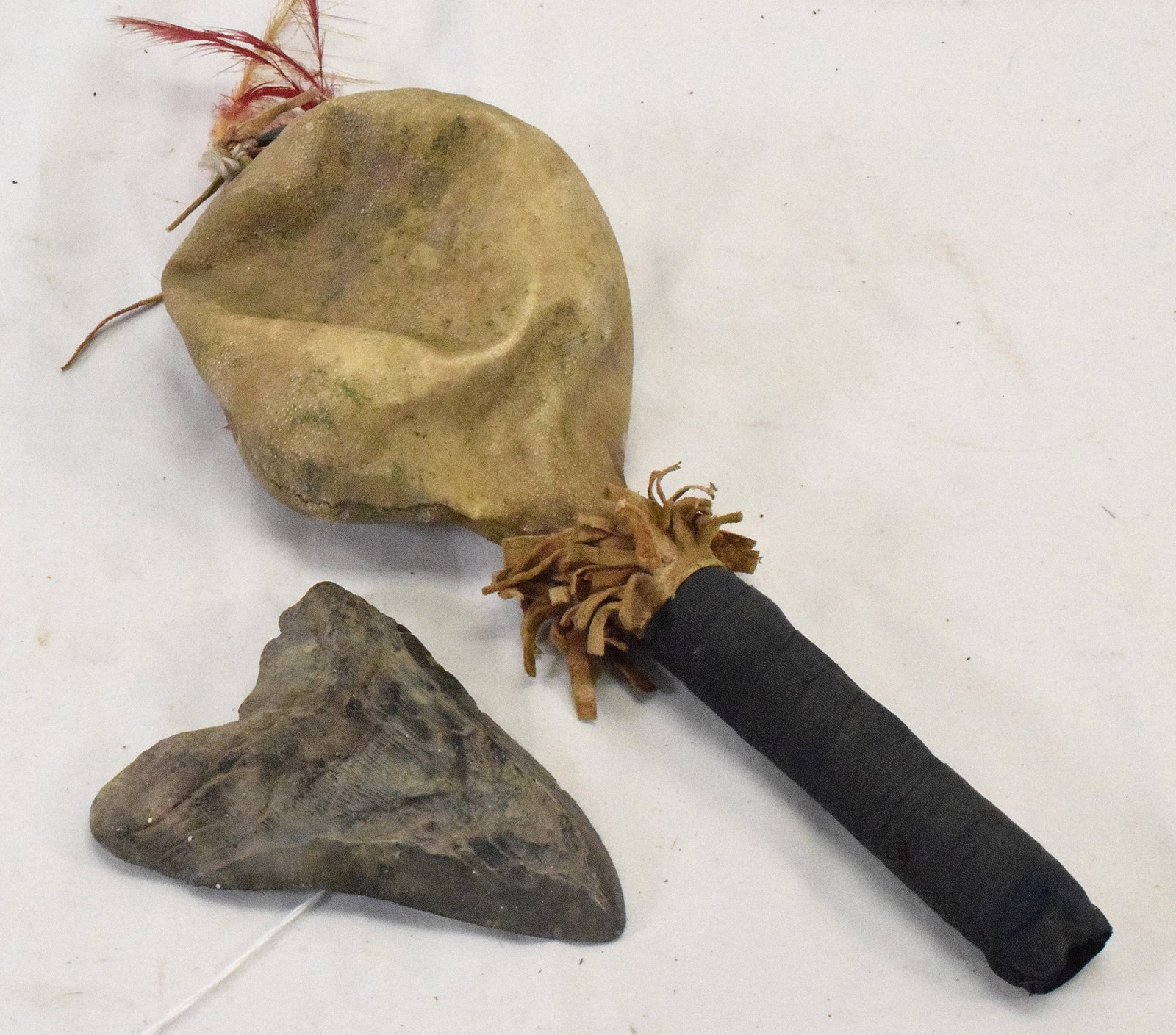 2 19TH INDIAN DANCE RATTLE AND SHARK TOOTH: Consists of 2 pieces. 1) 19th/20th Native American rattle. 12 inches long. Feather with tin cones on top. Hide rattle top with we believe seeds. Cloth wrapped handle. . 2) Fossilized megalodon sharkto