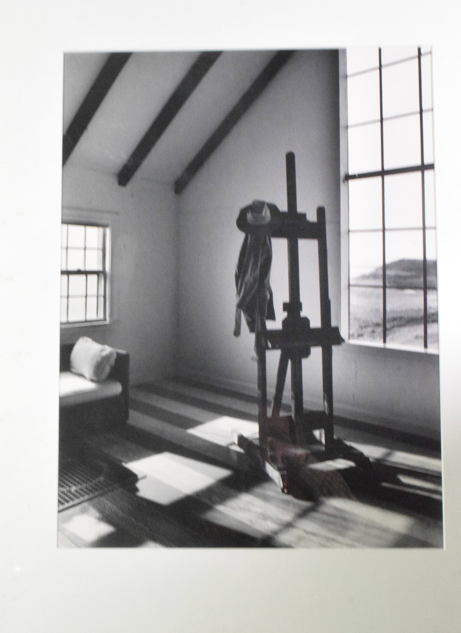 CLAIR FLANDERS BLACK & WHITE PHOTO EASEL: Claire Flanders black and white photo "Portugal the Studio" Image of artist's wood easel, hat and coat draped over it, view of landscape through the window. Signed on back , 5/25. Portugal, Cafe ?Edwa