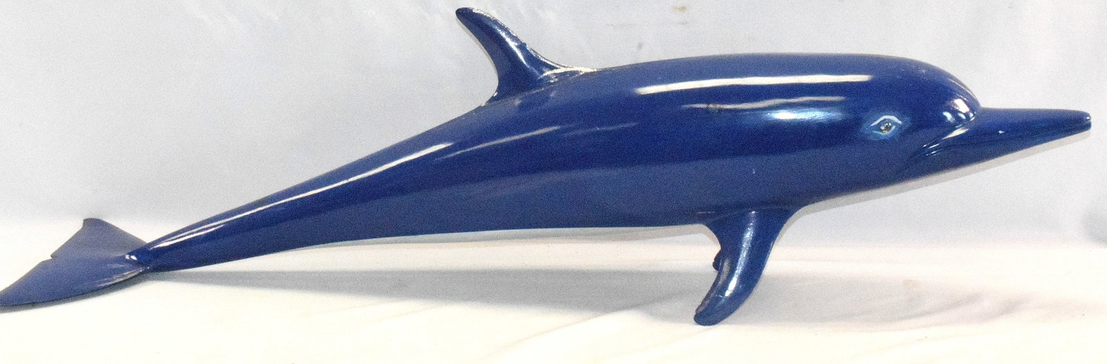 CARVED WOODEN DOLPHIN SCULPTURE: Sculpture is single wooden piece throughout the body. Midnight blue painted throughout body, underbelly is white, glass eyes and silver glaze running along fins and head. Crack on top of bodyto the