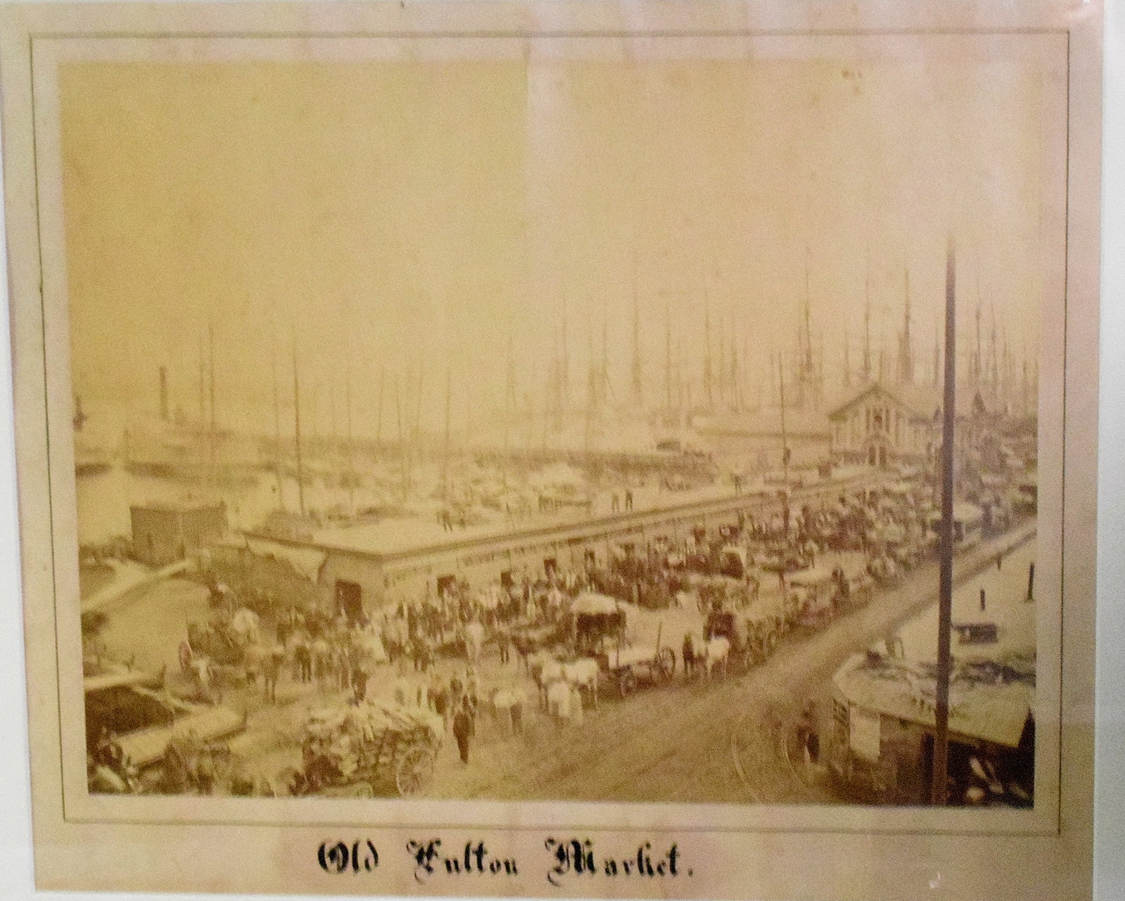 EARLY PHOTOGRAPH PRINT OF OLD FULTON MARKET: Early framed photogrph print of Old Fulton Market NY City, New York. Panoramic view, including the East River. Ca 1860's. Image 15 inches x 18 inches. Framed and matted under plexi glass. 23 x25 inche