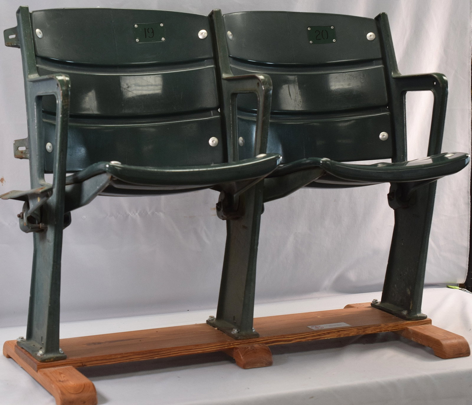 2 FENWAY PARK BLEACHER SEATS: Seats are green and part of a section, removed in 2007 from bleachers. Seats are numbered "19" and "20" and are mounted on a wooden foundation. Has plaque on bottom indicating year of removal
