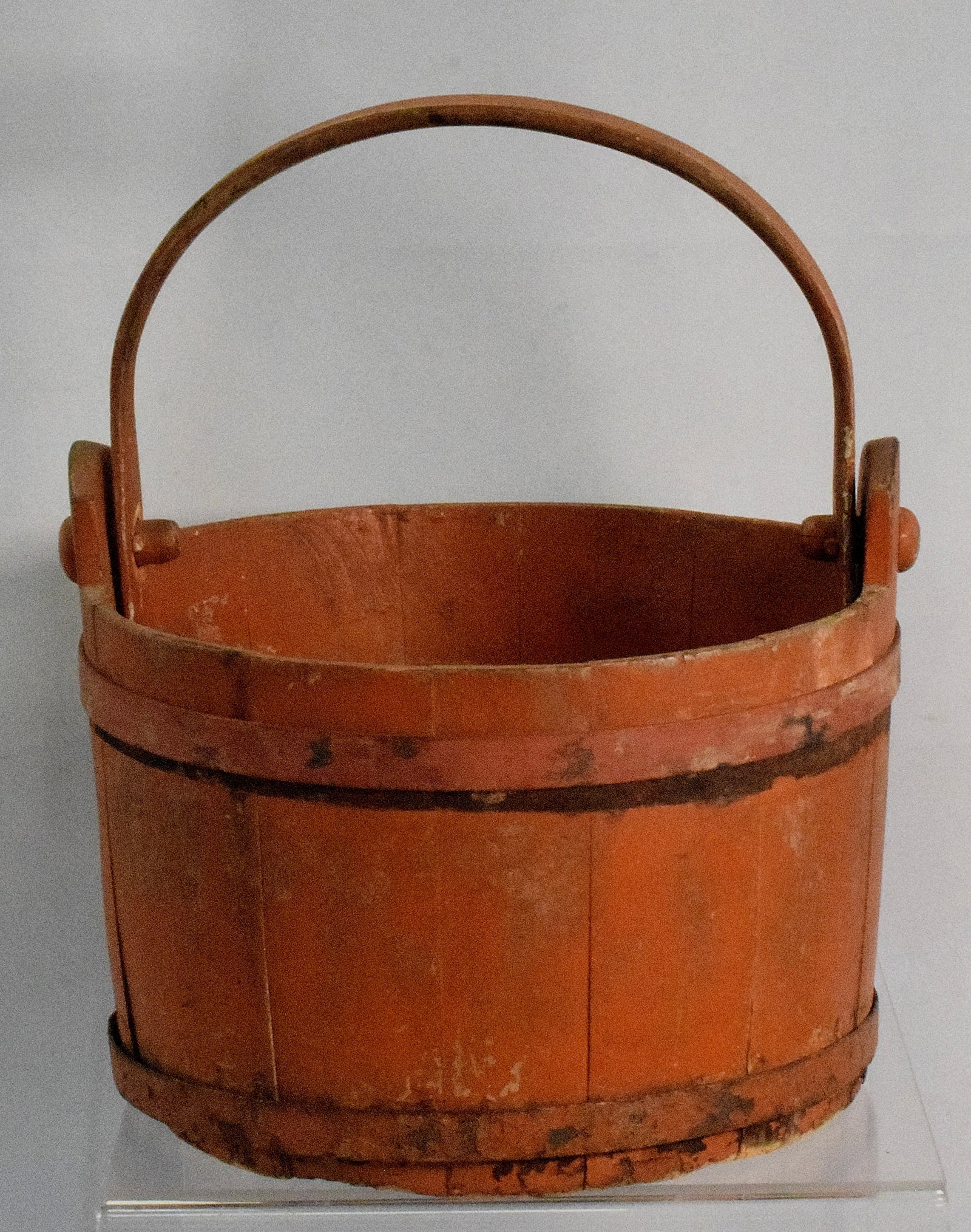 ORANGE PAINTED SHAVE BUCKET: Ca 19th century. American New England. Marked on bottom "P.R" "51" "P.V.". Shave construction with orange seems original except for top metal ring band. Swing handle. 10 1/4 inches diameter.