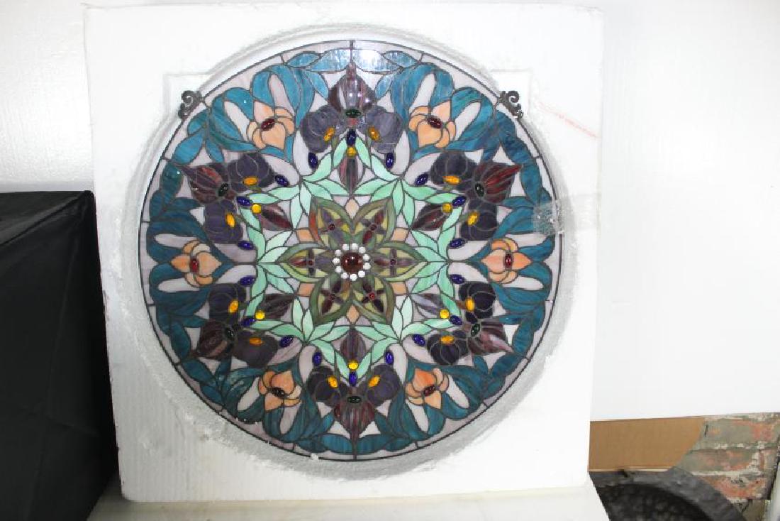 Watercott Glass Panel: This is a Watercott Glass Panel. It is in a circle shape, with floral designs facing inward to the main flower. The colors used are white, green, yellow, purple and red. There stones throughout the pa