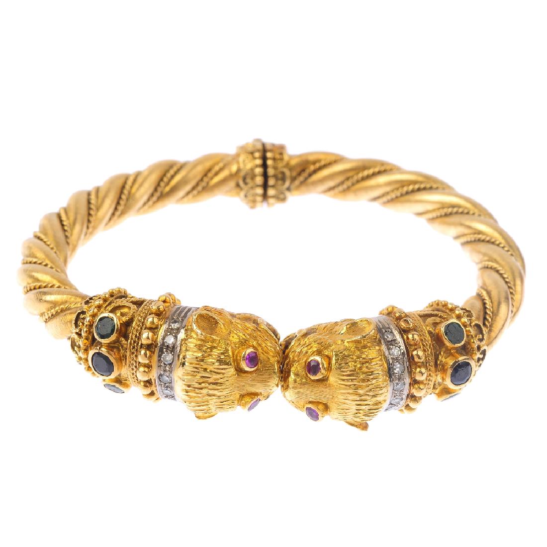 ILIAS LALAOUNIS - a diamond and gem-set double lion: ILIAS LALAOUNIS - a diamond and gem-set double lion head bangle. Comprising two lion mask terminals, with ruby eyes, diamond collar and sapphire, emerald and cannetille sides, to the rope-twist and sp