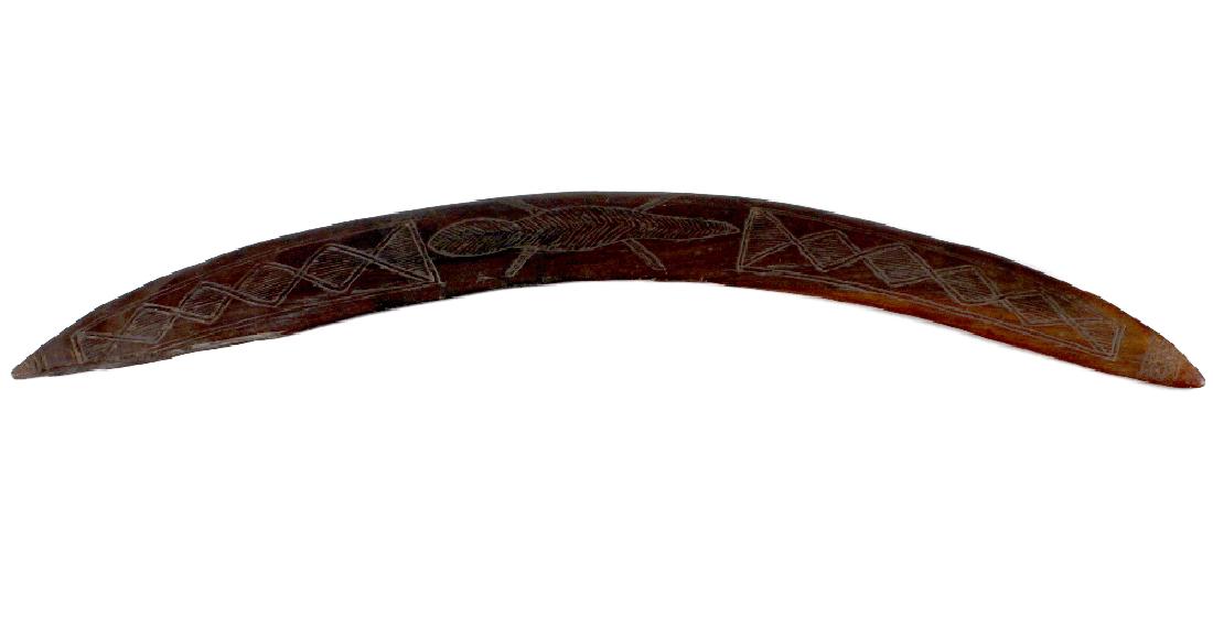 An Australian Aboriginal stone-carved hardwood: An Australian Aboriginal stone-carved hardwood boomerang. The curved upper face incised with a lizard between conjoined lozenges, 28, (71cm) along outer curve, (s/d).