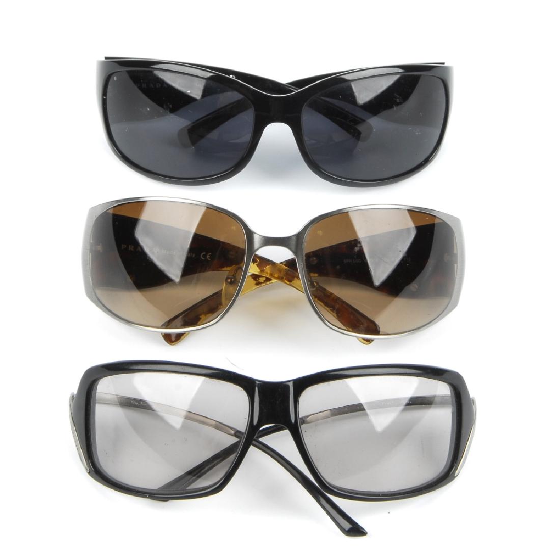 Three pairs of designer sunglasses. To include two: Three pairs of designer sunglasses. To include two pairs of Prada sunglasses of a similar style with inlaid swirl detailing to each temple side, together with a pair of Max Mara sunglasses with very l