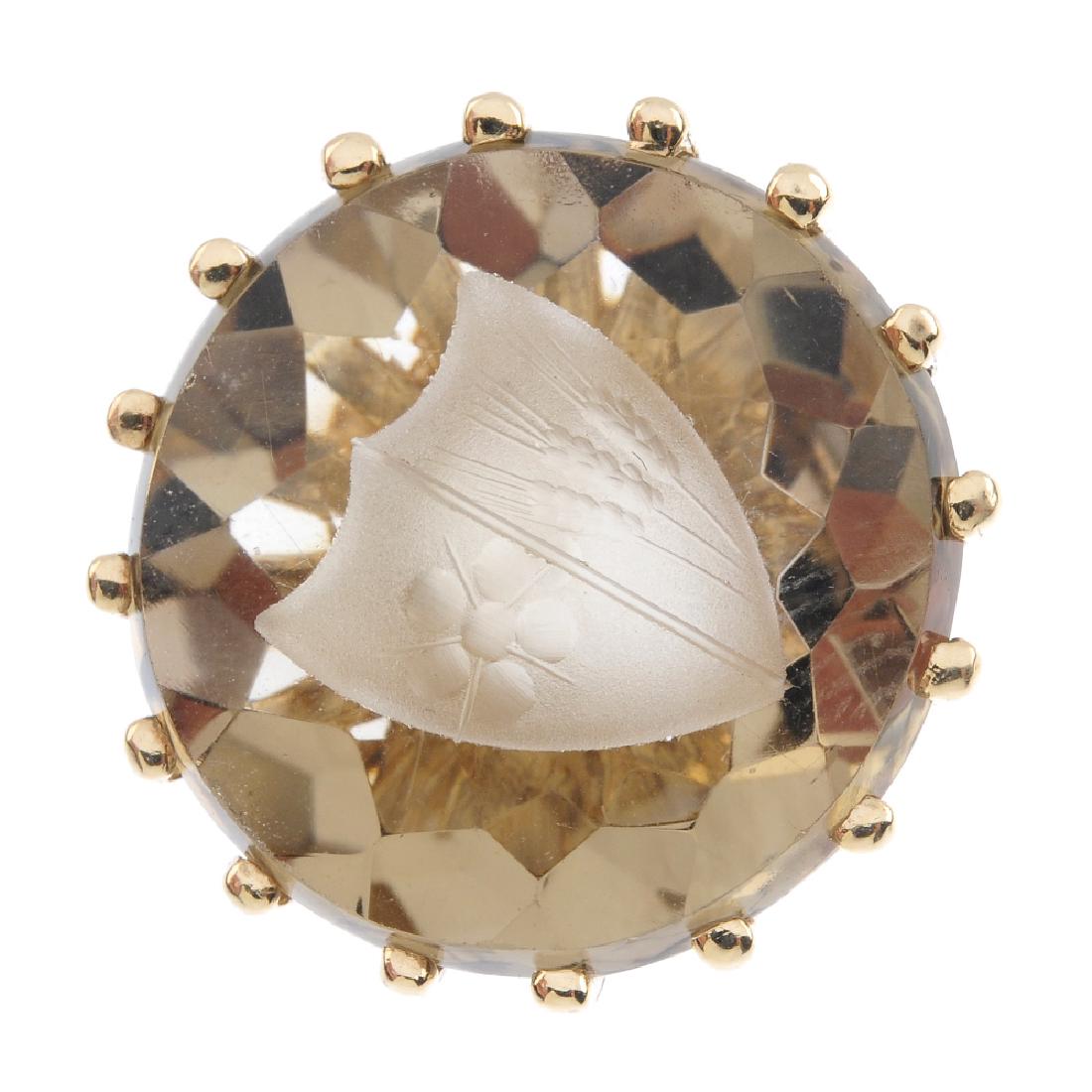 A gold smoky quartz signet ring. The circular smoky: A gold smoky quartz signet ring. The circular smoky quartz intaglio, carved to depict a coat-of-arms, with grooved band. Hallmarks partially indistinct. Ring size M. Weight 8.9gms.