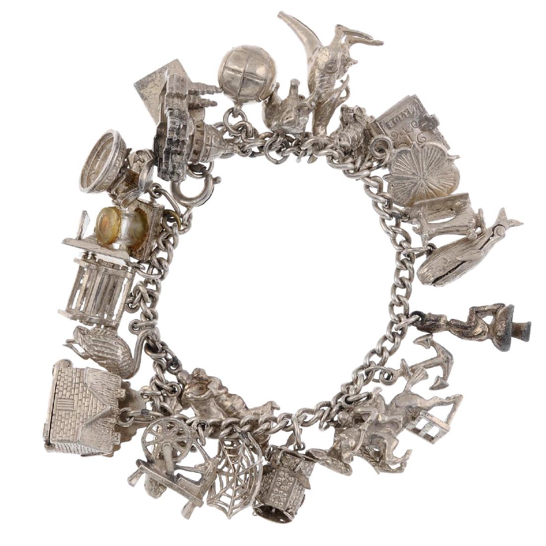 A silver charm bracelet with charms. The curb-link: A silver charm bracelet with charms. The curb-link chain with spring-ring clasp suspending twenty-six charms including a whale charm, with mouth opening to reveal figures within, a spinning wheel and 