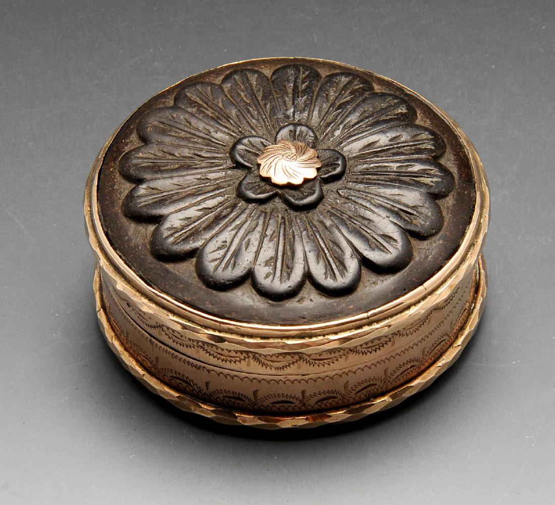 A small trinket box, of circular lidded form with: A small trinket box, of circular lidded form with carved organic base and cover (possibly wood) and engraved mounts, opening to reveal tortoiseshell lined interior. Appears unmarked, the mounts of bot