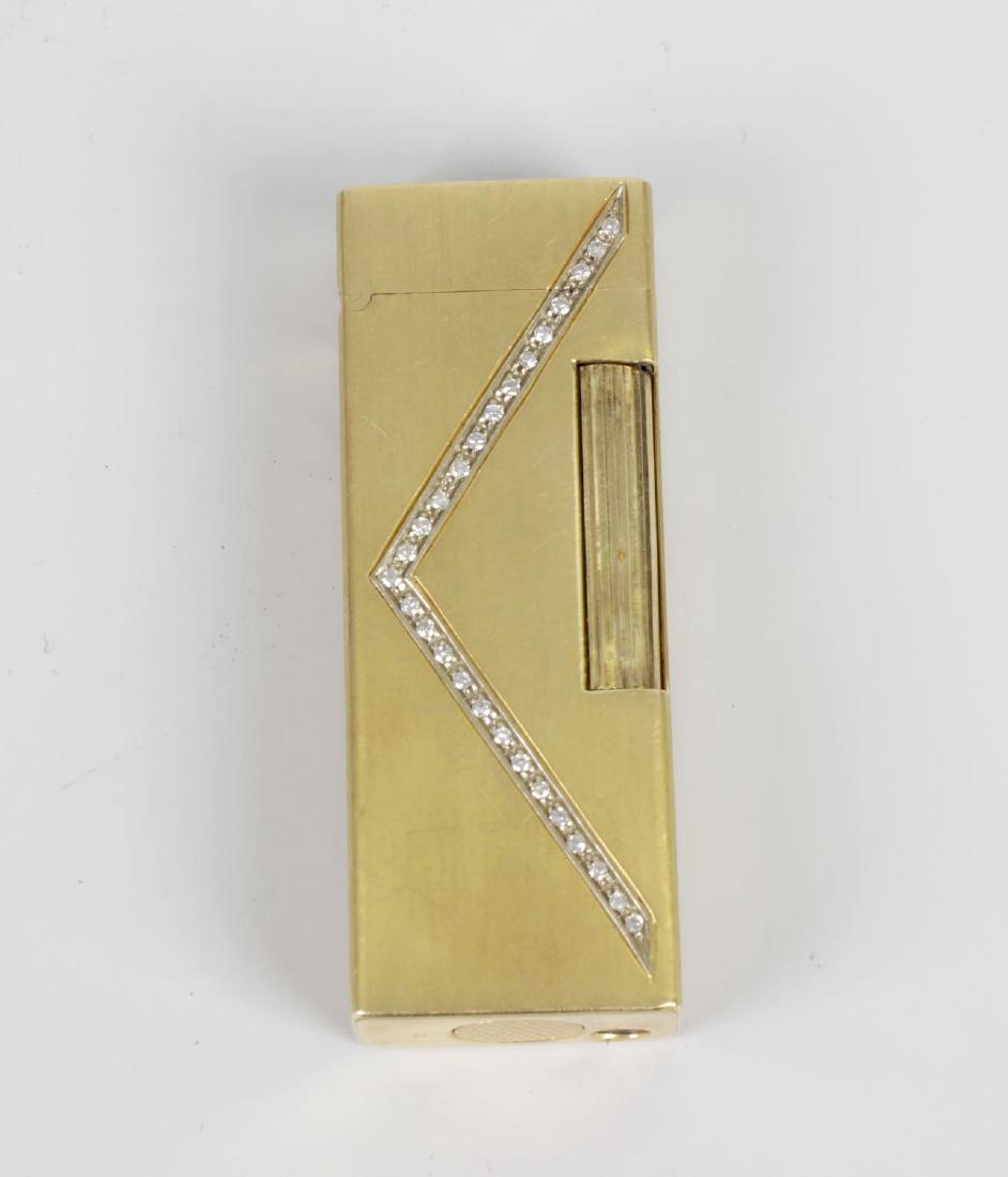 An 18k yellow metal lighter. Of 'Rollagas' type: An 18k yellow metal lighter. Of 'Rollagas' type attributed to Dunhill, the oblong body later-set with a a V-shaped line of small diamonds, stamped beneath '750', marked 'Dunhill' beneath cover only, 2