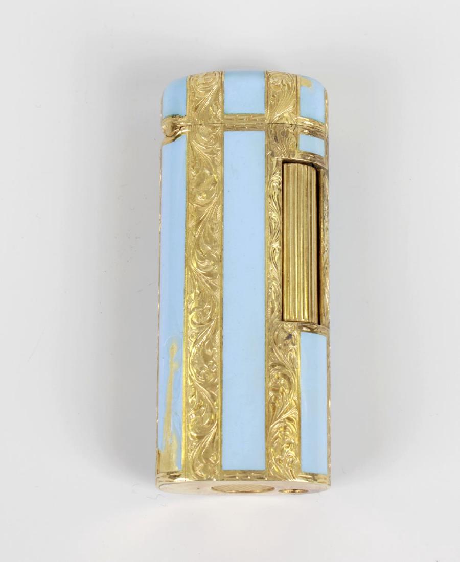 An 18k yellow metal and blue enamel lighter. The oval: An 18k yellow metal and blue enamel lighter. The oval section body of Rollagas type, with alternate strips of foliate engraving and pale blue enamel (losses), stamped beneath '750', marked 'Dunhill' b