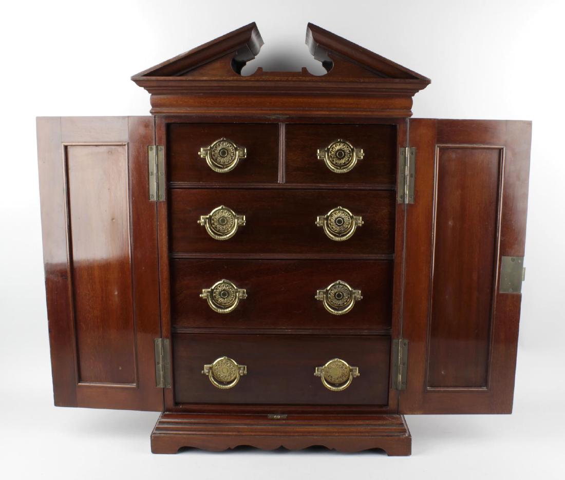 A good quality late Victorian or Edwardian collector's: A good quality late Victorian or Edwardian collector's mahogany cabinet. In the form of a miniature double wardrobe, the architectural broken pediment over fielded paneled doors, each with carved swag
