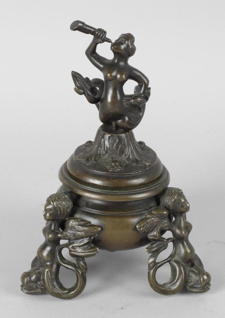 A bronze inkwell and cover of Neo Classical form, the: A bronze inkwell and cover of Neo Classical form, the domed cover with finial modelled as a mermaid, the base upon three cast supports modelled as winged females and dolphins, 7 (18cm) high.