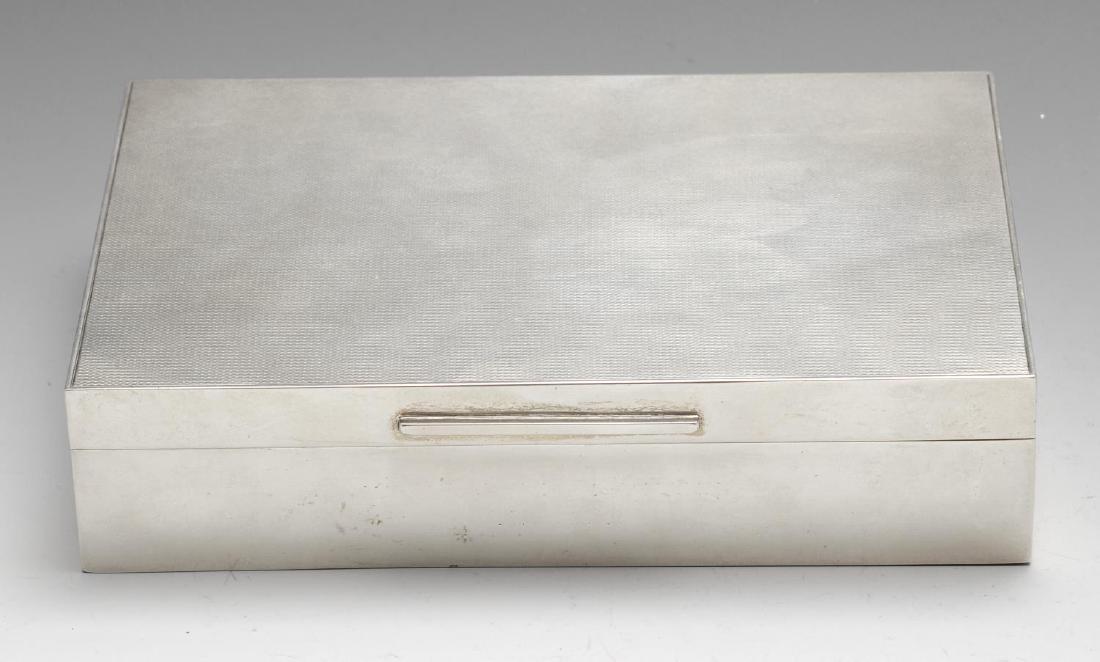 A silver mounted table cigarette box, of rectangular: A silver mounted table cigarette box, of rectangular form with engine-turned hinged lid, opening to reveal a wood lined interior with two compartments. Hallmarked Padgett & Braham Ltd., London, date l