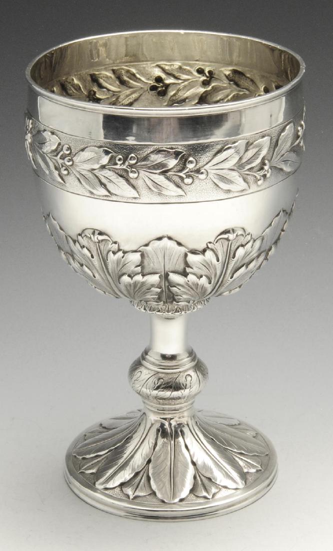 A silver goblet or chalice, the circular bowl with: A silver goblet or chalice, the circular bowl with moulded rim above a raised band of laurel leaves against a stippled ground, and a wide acanthus leaf border to the lower section, raised on a knopped