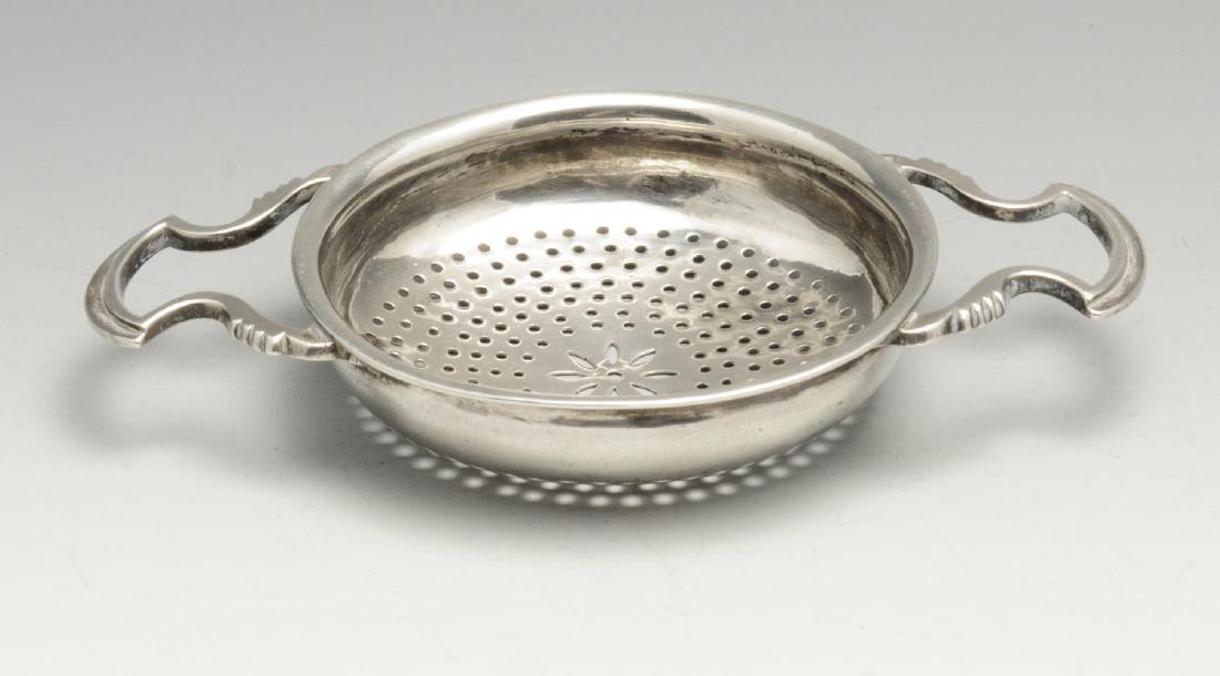 A twin-handled lemon strainer, possibly Georgian, of: A twin-handled lemon strainer, possibly Georgian, of circular form with pierced bowl and applied scroll handles. Indistinctly marked to the bowl. Maximum width inclusive of handles measuring 6 inches 