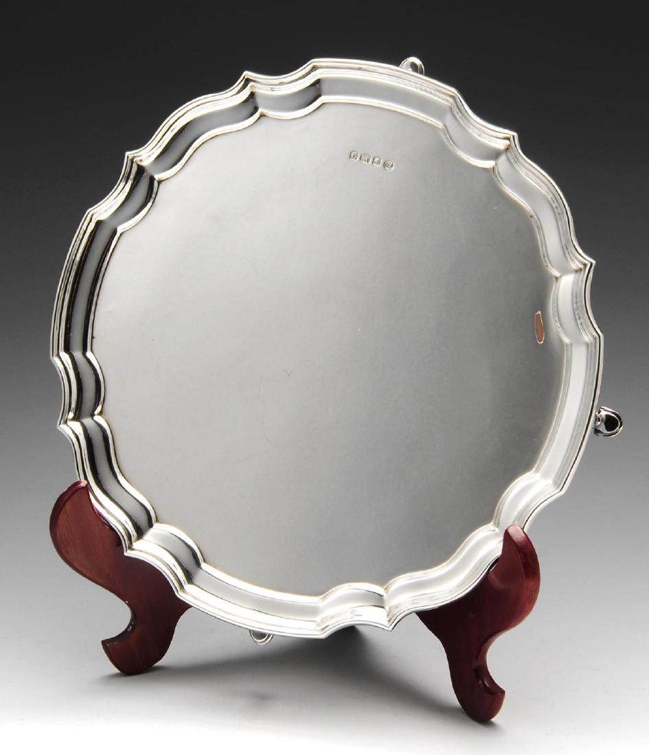A modern silver salver, of plain circular form with: A modern silver salver, of plain circular form with scalloped edge border and raised upon four hoof feet. Hallmarked Francis Howard Ltd., Sheffield 1973. Diameter measures 10 inches (25.5 cm), weight 