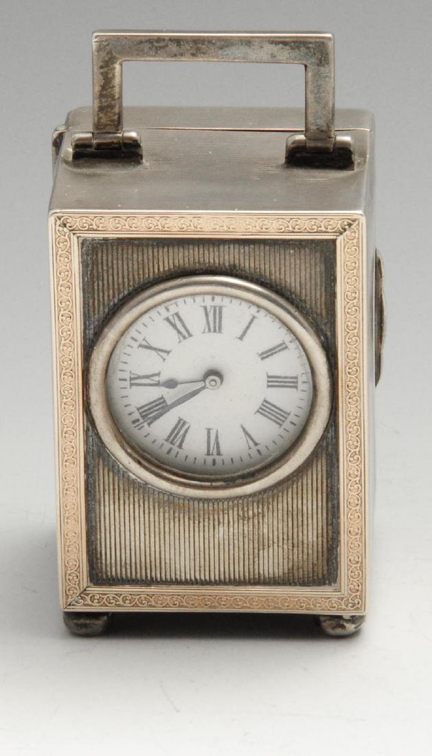 An early twentieth century silver mounted carriage: An early twentieth century silver mounted carriage clock, the engine-turned rectangular form with applied gold tone foliate border to front, with hinged angular carry handle and the whole raised on fo