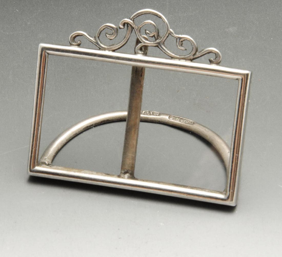 An Edwardian silver menu or name card holder, the open: An Edwardian silver menu or name card holder, the open rectangular frame with glass insert and foliate scroll surmount, and semi-circular stand. Hallmarked to stand Cornelius Desormeaux Saunders & Jam