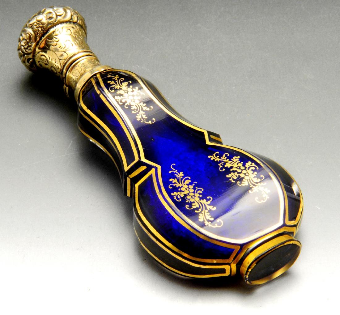 A French silver-gilt mounted blue glass scent bottle,: A French silver-gilt mounted blue glass scent bottle, the hinged lid engraved and chased with foliate motifs and stippled decoration to the neck mount, the ogee shape blue glass body gilded with flora