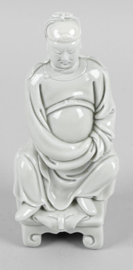A Chinese porcelain figure modelled as Guan Gong,: A Chinese porcelain figure modelled as Guan Gong, finished in a grey tone glaze, dressed in robes and seated upon a throne, 5.5 (14cm) high.
