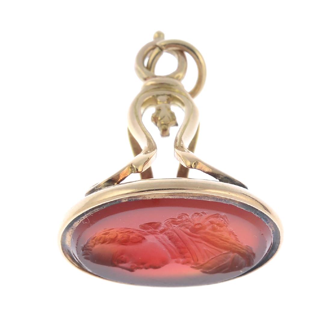 A mid 20th century gold carnelian fob. The oval: A mid 20th century gold carnelian fob. The oval carnelian panel, carved to depict a gentleman in profile, to the scrolling pedestal and plain surmount hoop. Length 2.7cms. Weight 4.7gms.