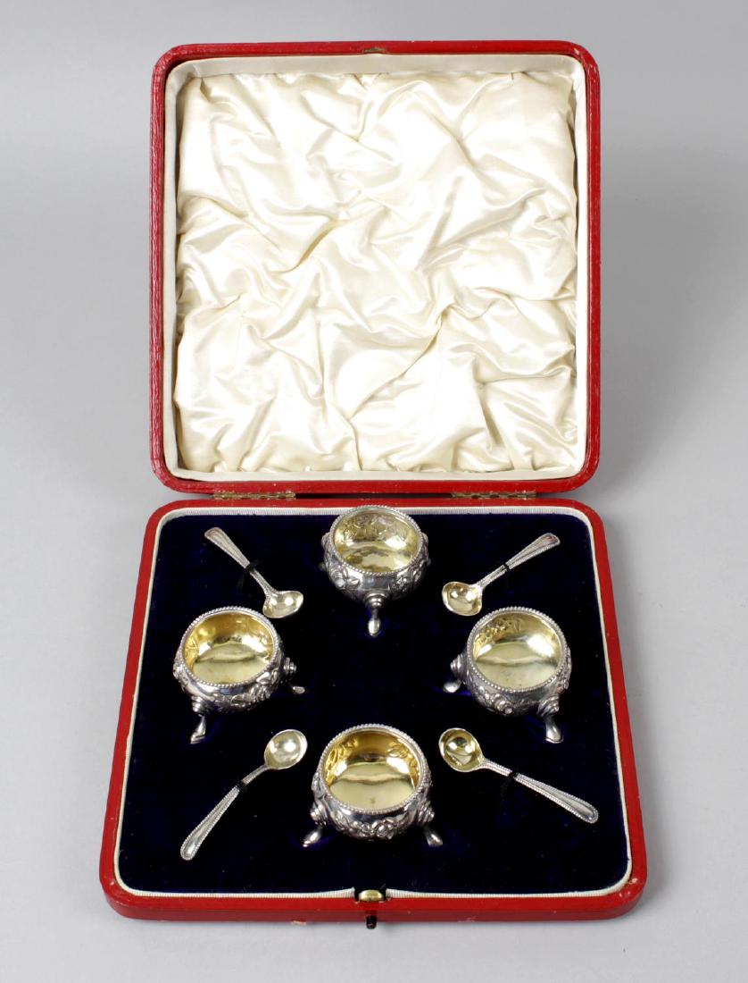 A cased mid-Victorian silver set of four open salts and: A cased mid-Victorian silver set of four open salts and spoons, each floral embossed circular salt with beaded rim, gilt interior and raised on four stepped hoof feet, salt spoons also with bead borde