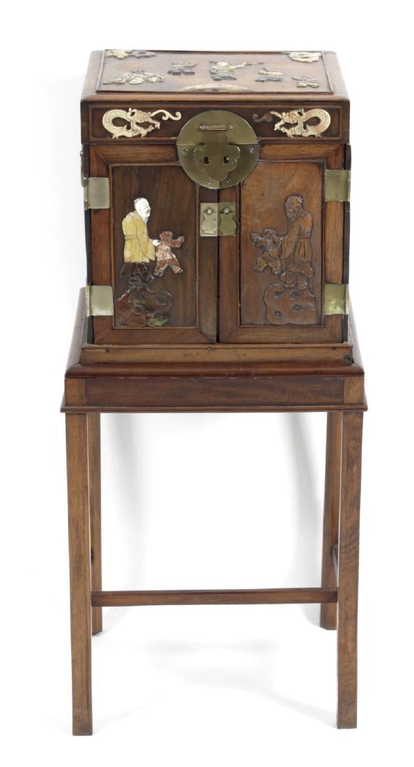 An Oriental hardwood cabinet, the lift up hinged top: An Oriental hardwood cabinet, the lift up hinged top above a front fitted with twin doors, opening to reveal an interior fitted with an arrangement of drawers, the whole with applied soapstone, ivory 