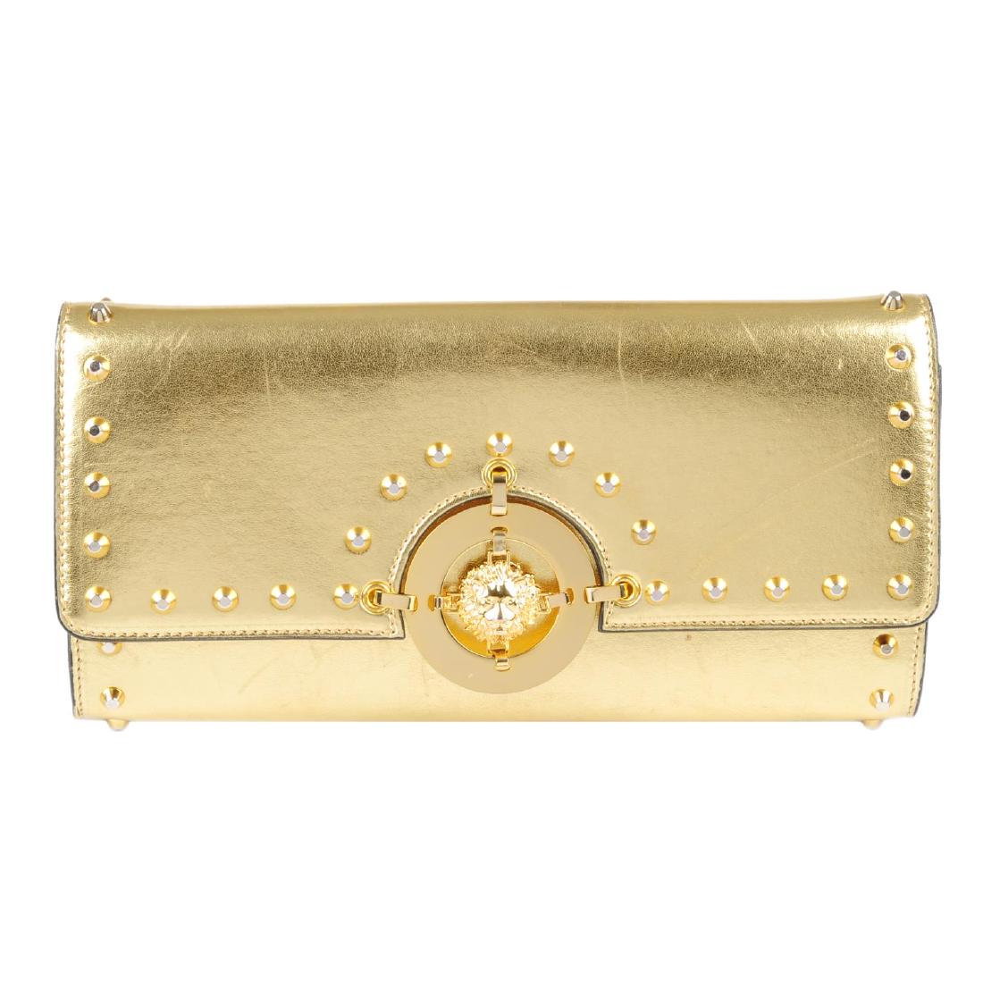 VERSUS BY VERSACE - a gold leather clutch. Crafted from: VERSUS BY VERSACE - a gold leather clutch. Crafted from metallic gold leather, with gold-tone studded trim and lion medallion to the centre, hidden magnetic snap fastening, optional chain strap and li