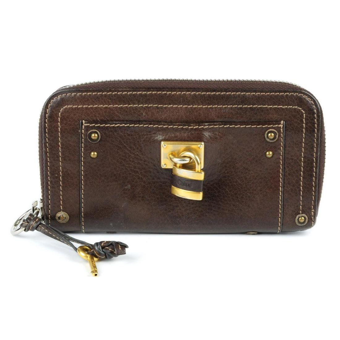CHLOÉ - a brown leather Paddington wallet. Crafted from: CHLOÉ - a brown leather Paddington wallet. Crafted from grained brown leather, featuring a gold-tone lock detail, silver-tone wraparound zip with card, note and zip pockets. Measuring 2.5 by 10 by 19